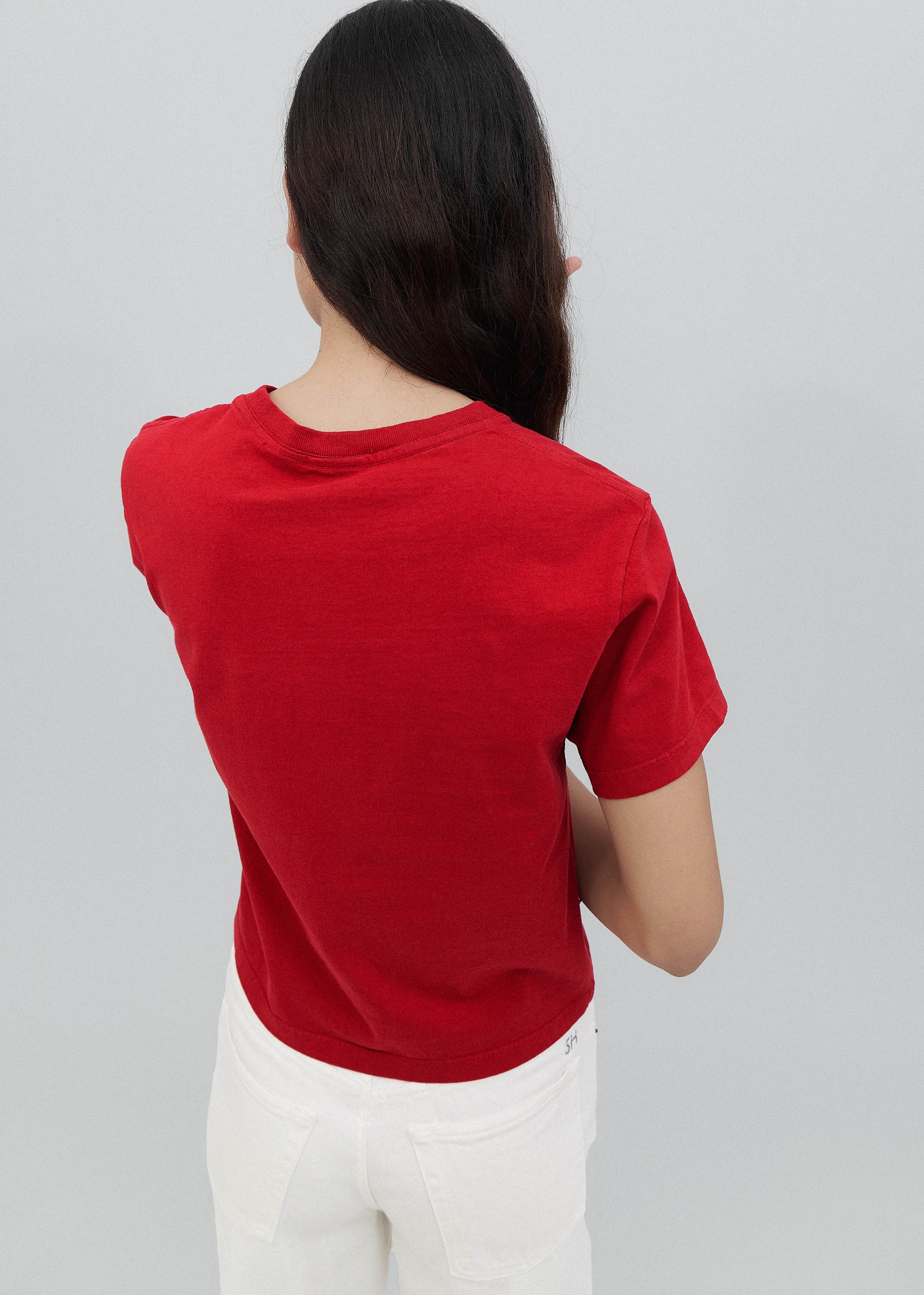 Person wearing a red t-shirt and white pants on a plain background