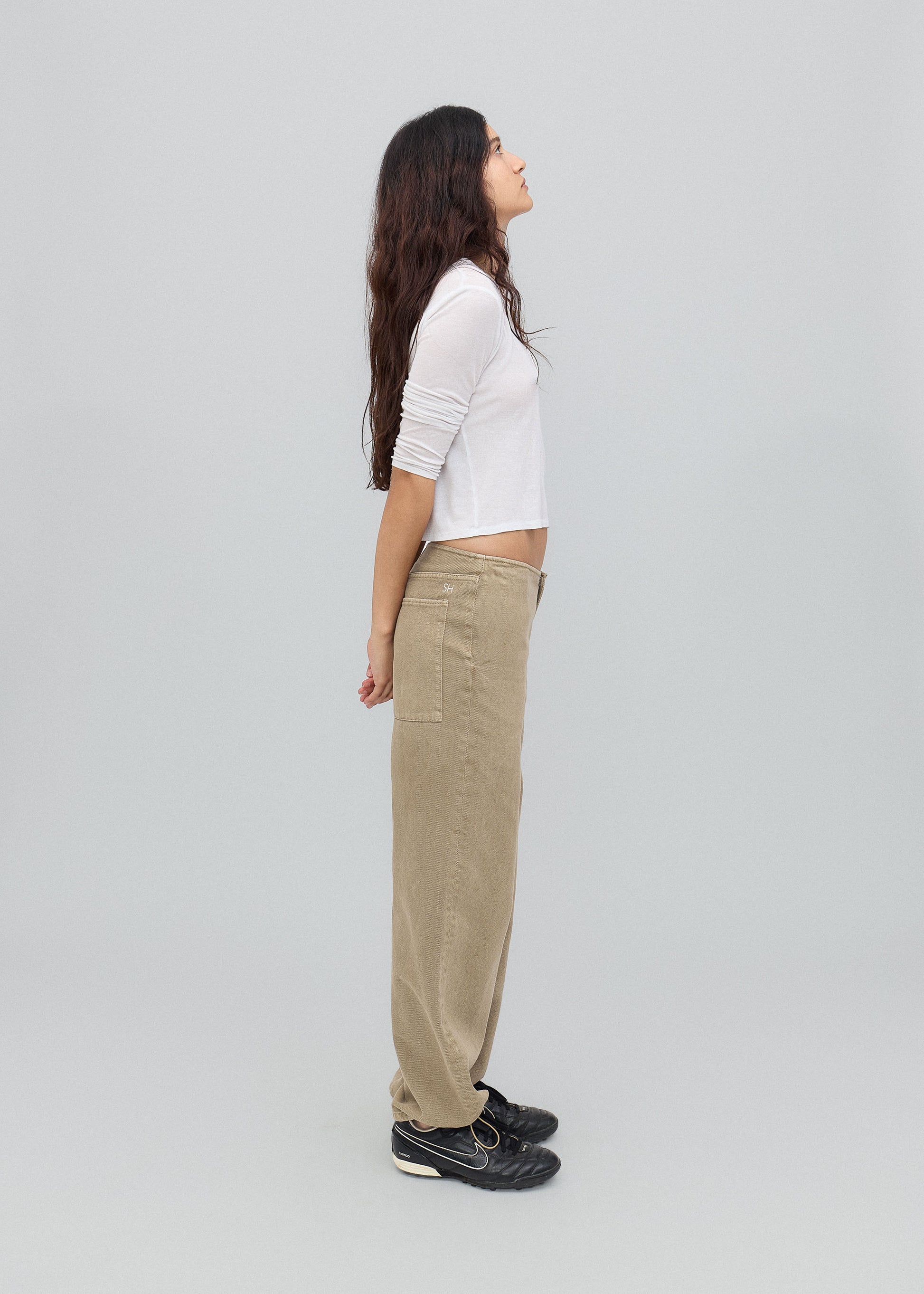 Woman wearing a white top and beige pants standing against a light gray background