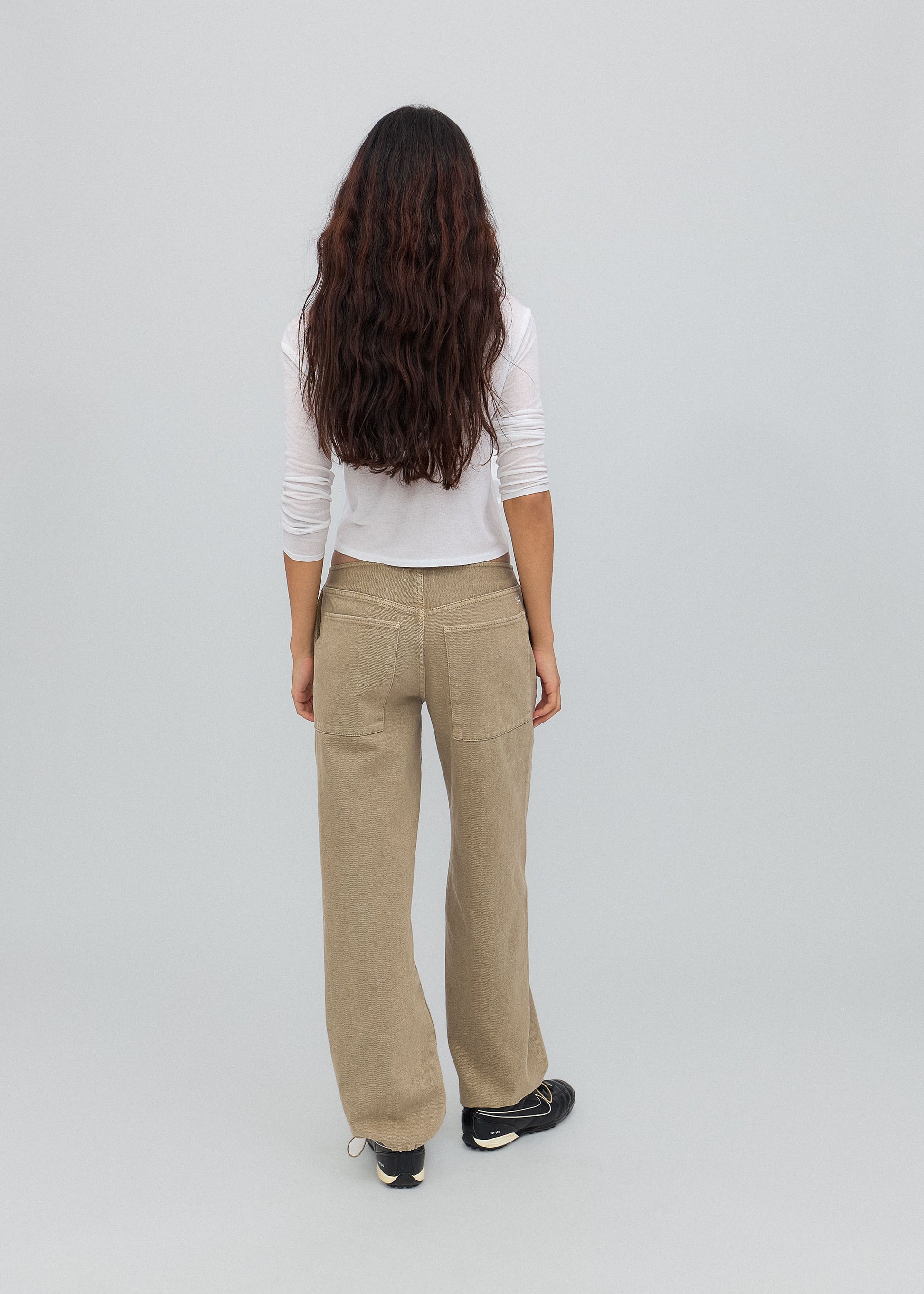 Person wearing beige pants and a white top on a light gray background