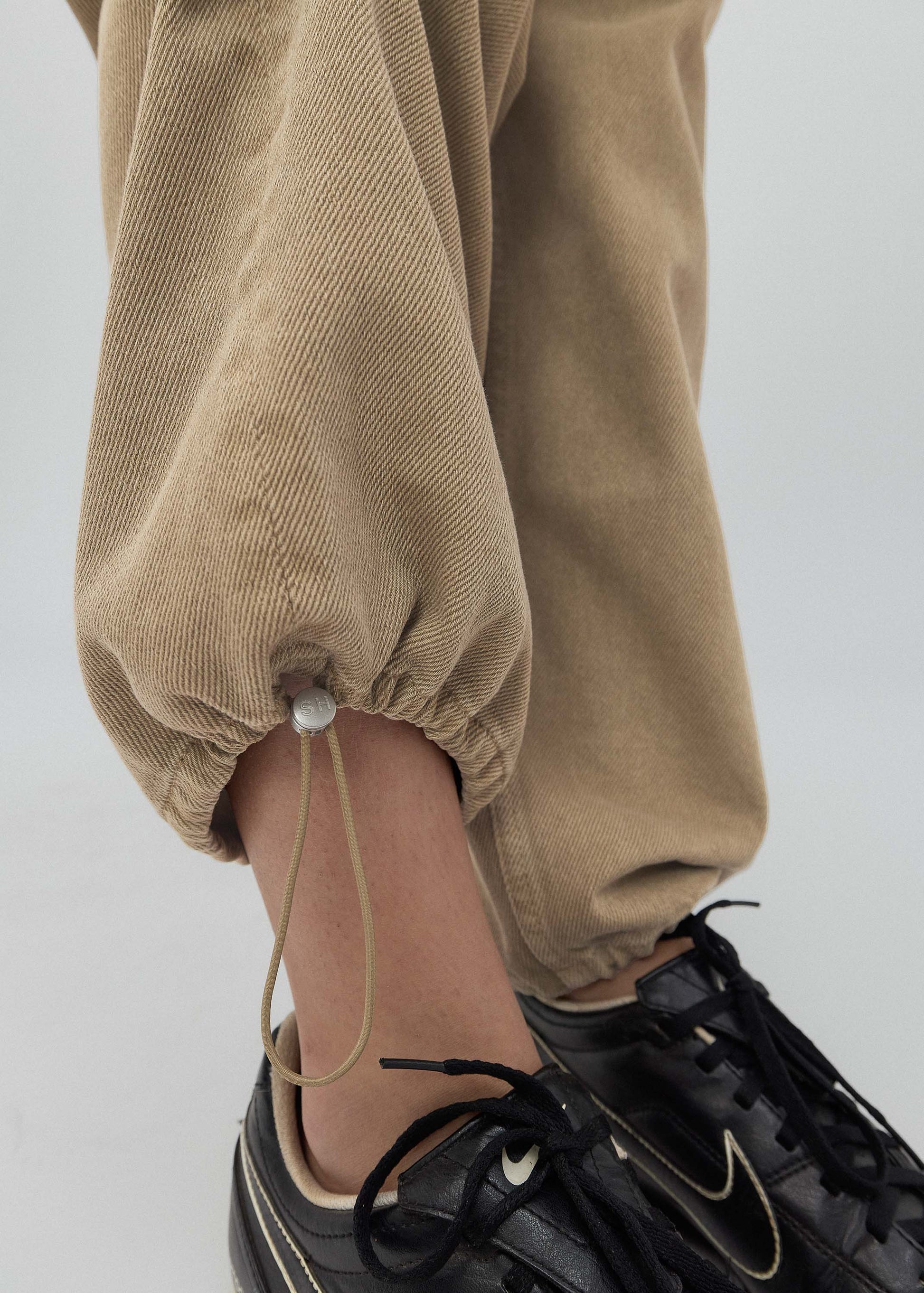 Close-up of brown pants and black sneakers on a plain background