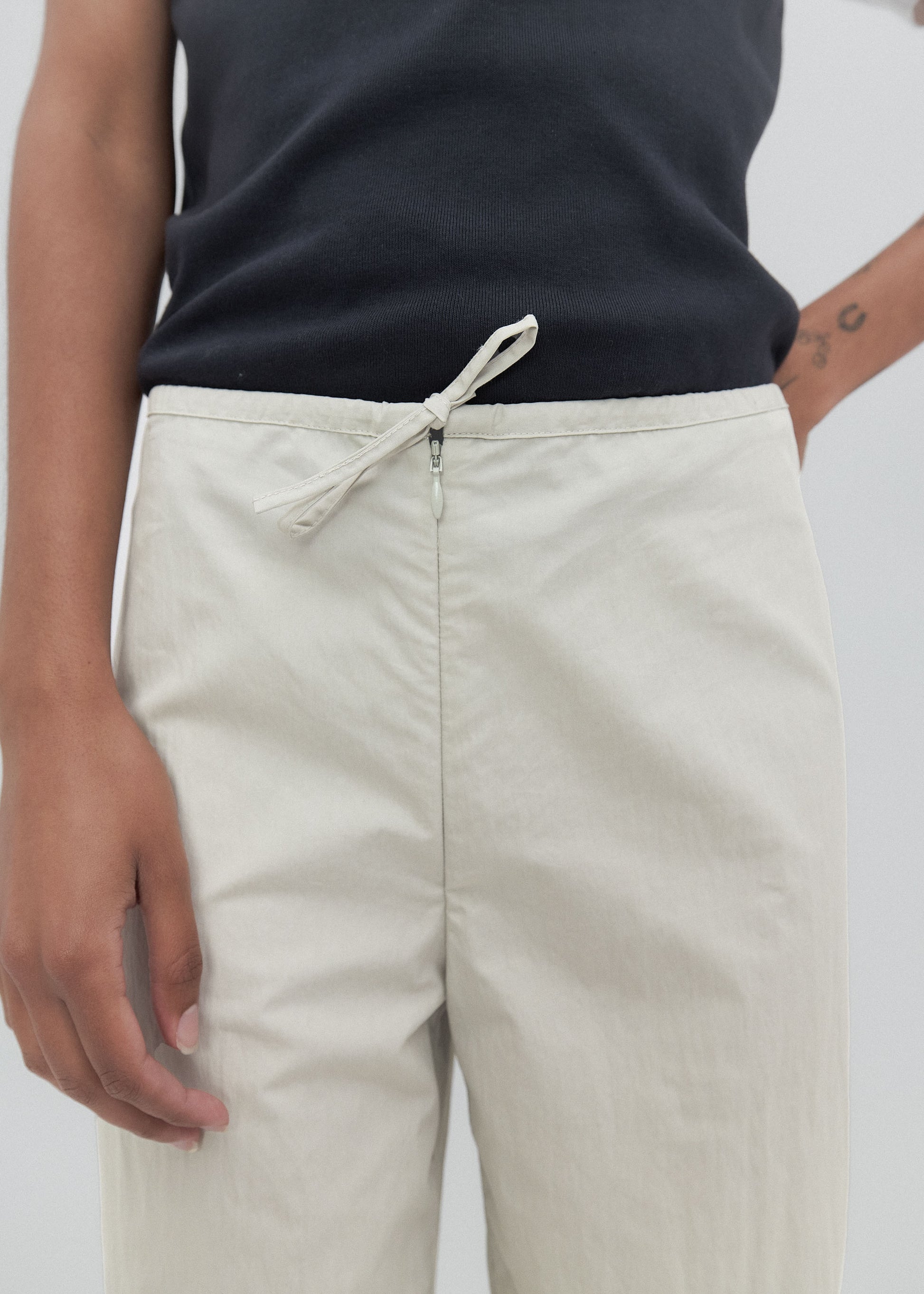 Person wearing beige pants and a black top on a white background