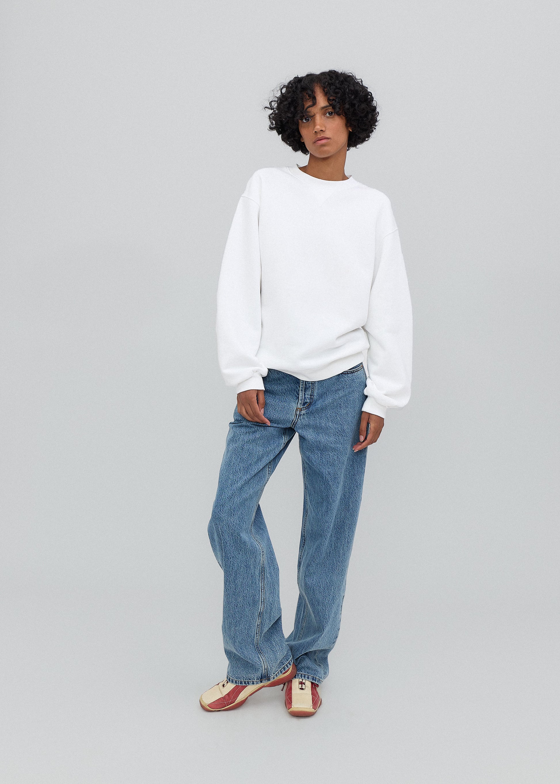 Person wearing a white sweater and blue jeans on a gray background