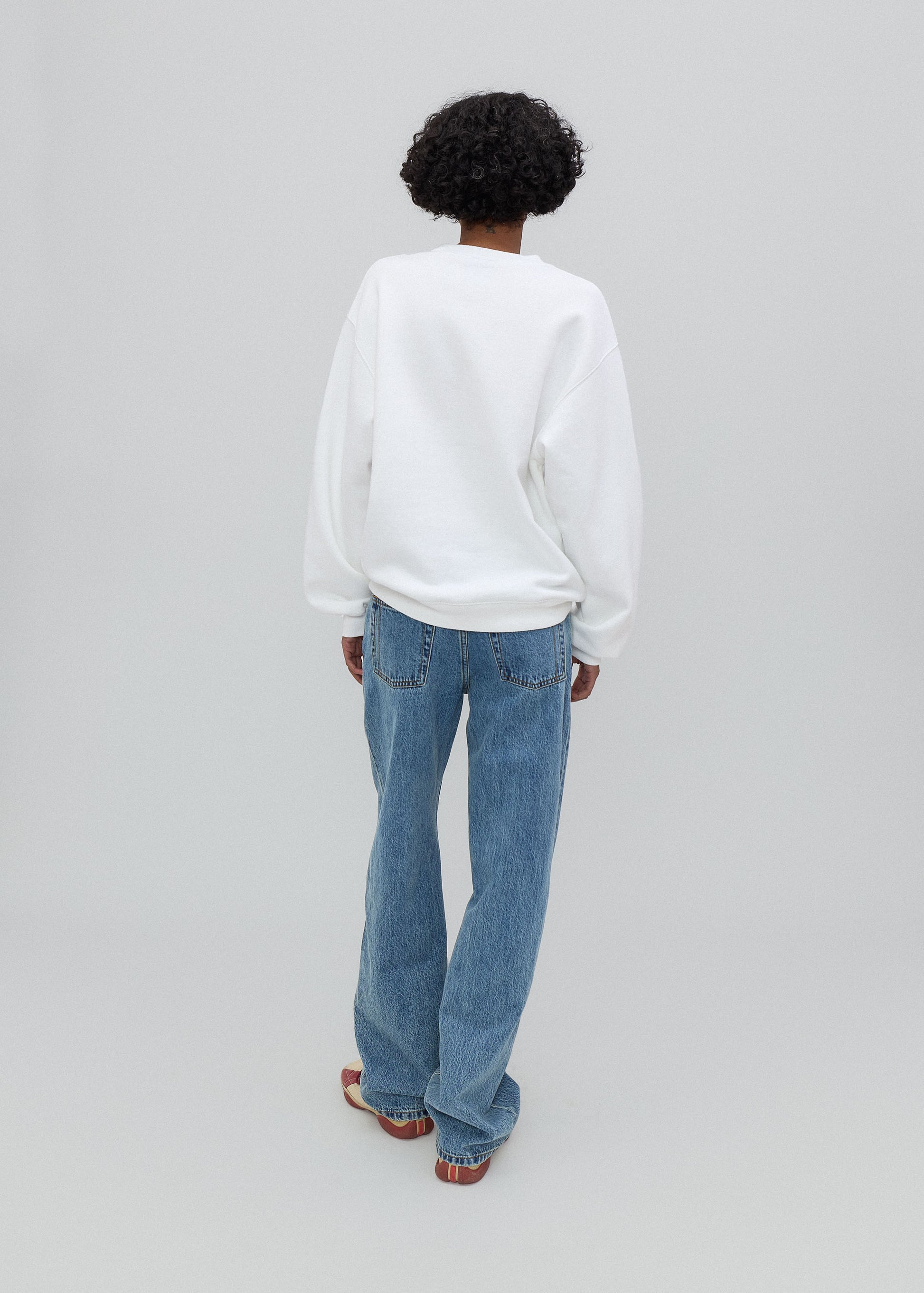 Person wearing a white sweatshirt and blue jeans on a gray background