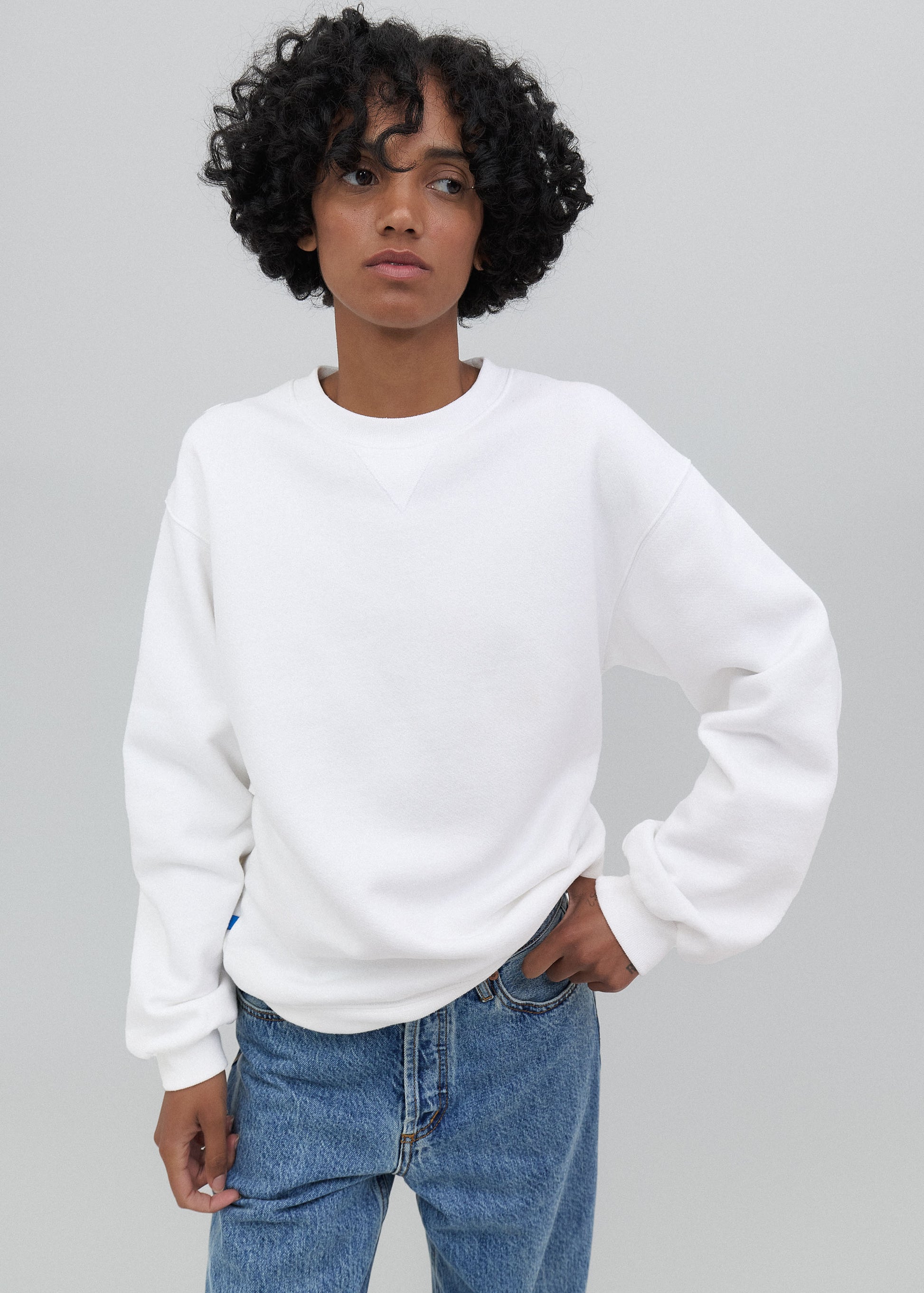 Person wearing a white sweatshirt and blue jeans against a gray background