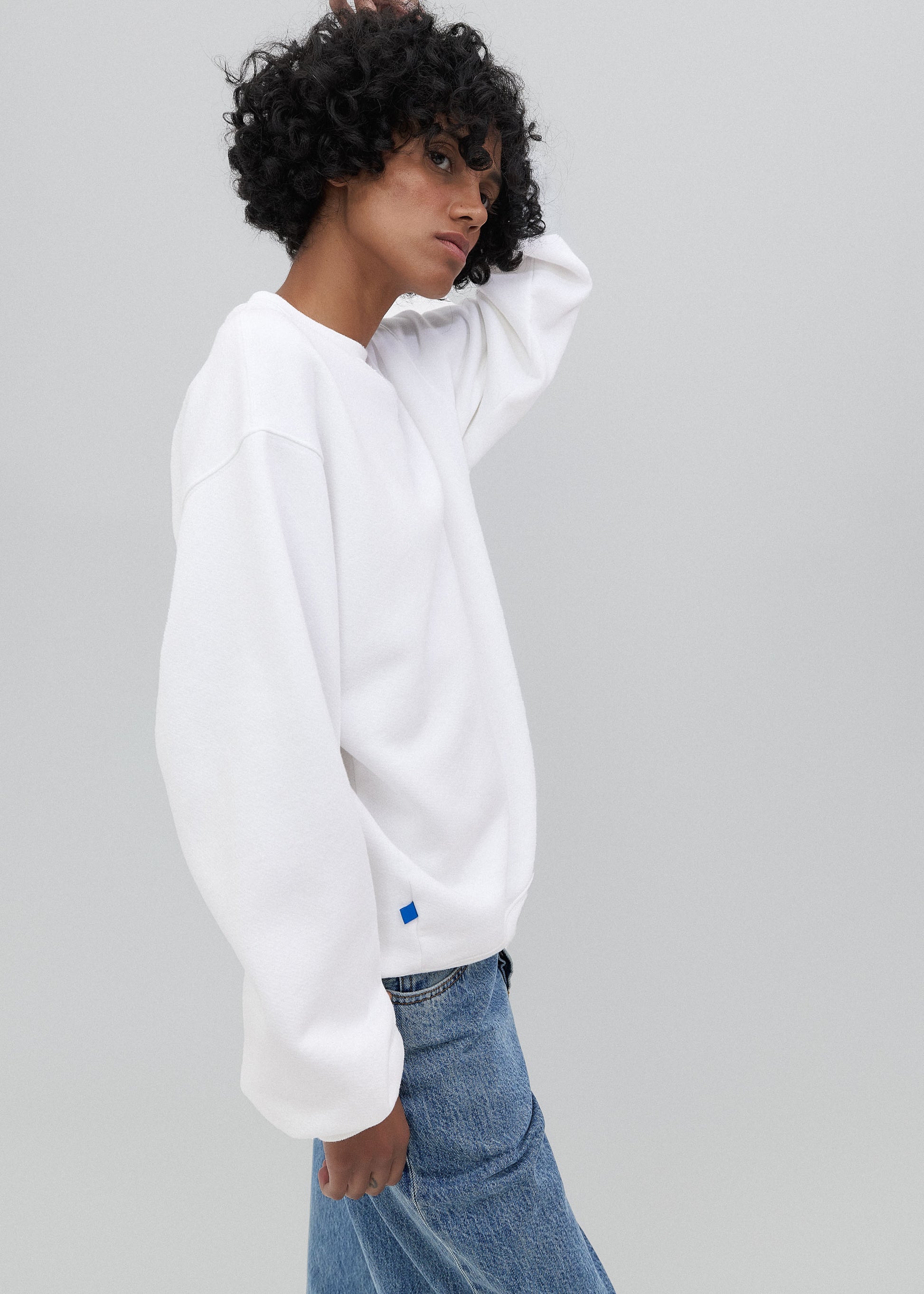 Person wearing a white sweatshirt with a small logo on a gray background