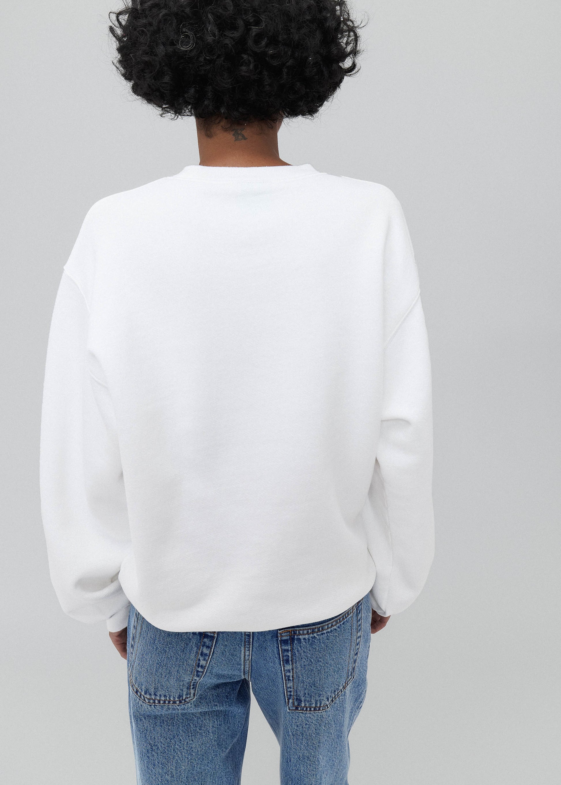Person wearing a white sweatshirt and blue jeans on a gray background