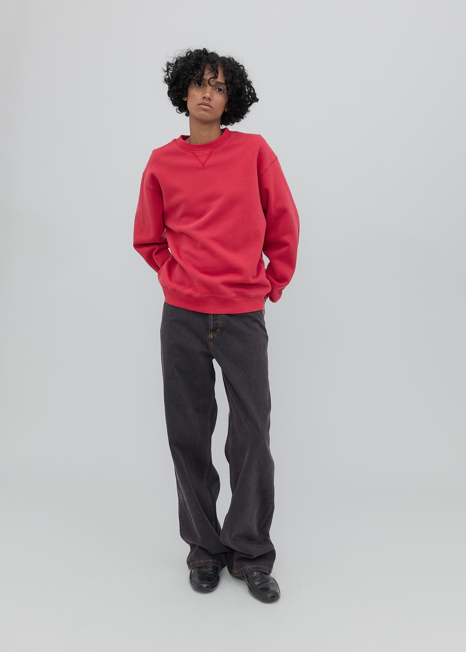 Person wearing a red sweater and black pants on a light gray background