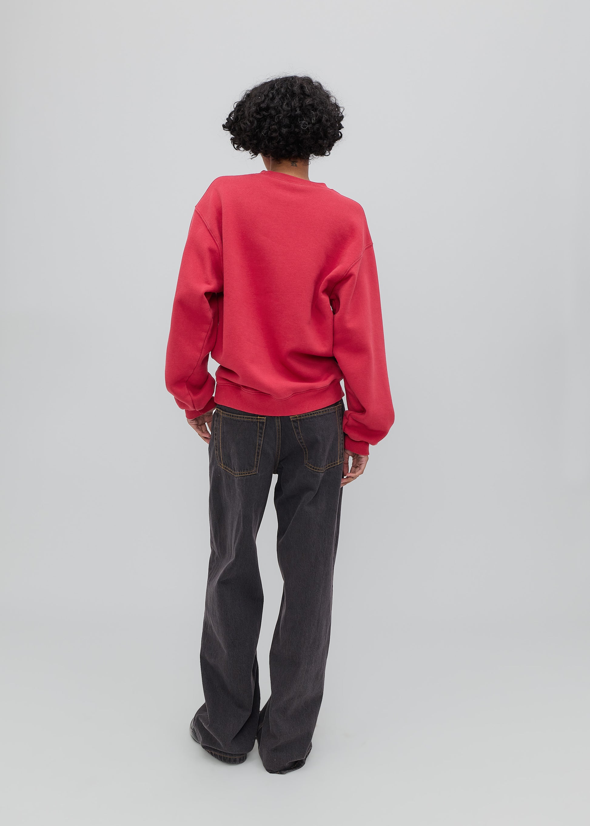 Person wearing a red sweatshirt and dark jeans on a light gray background