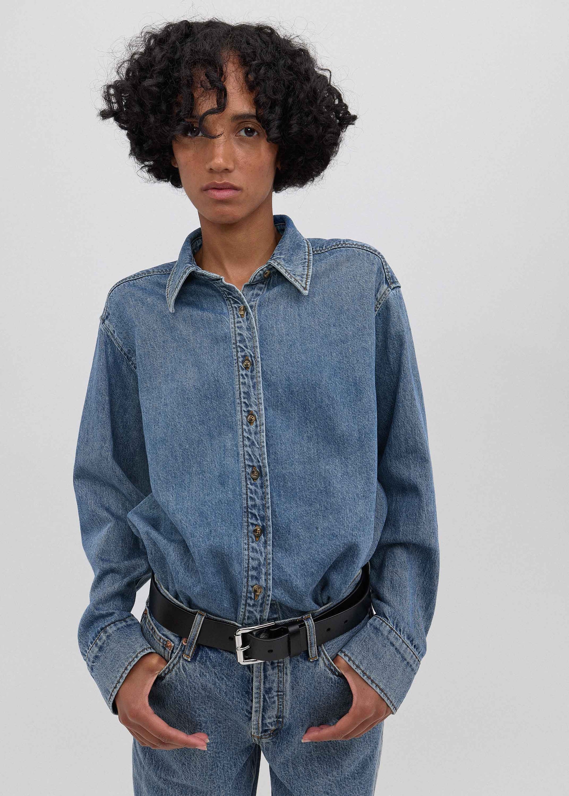 Person wearing a blue denim shirt and jeans on a plain background