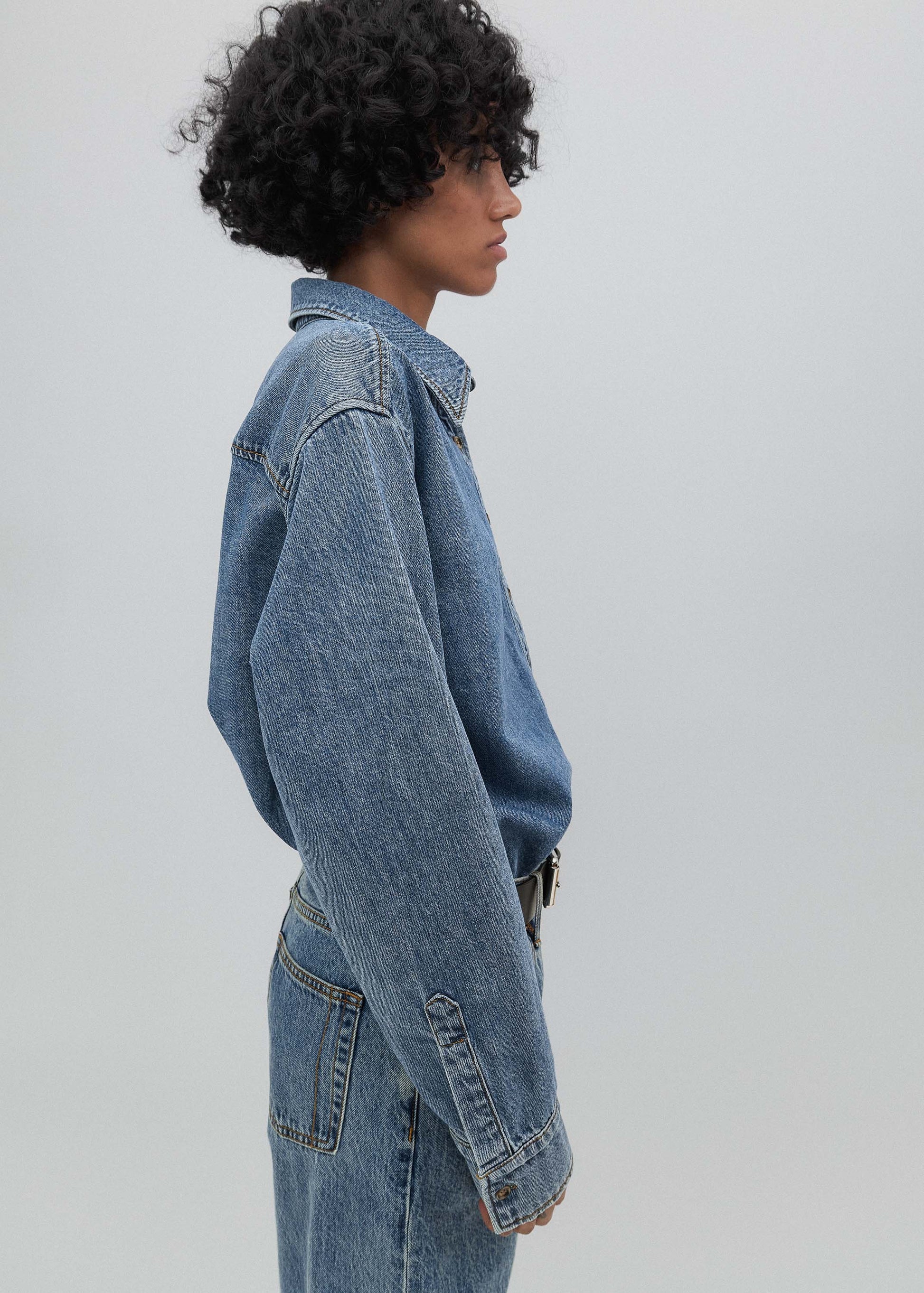 Person wearing a blue denim jacket and jeans on a plain background
