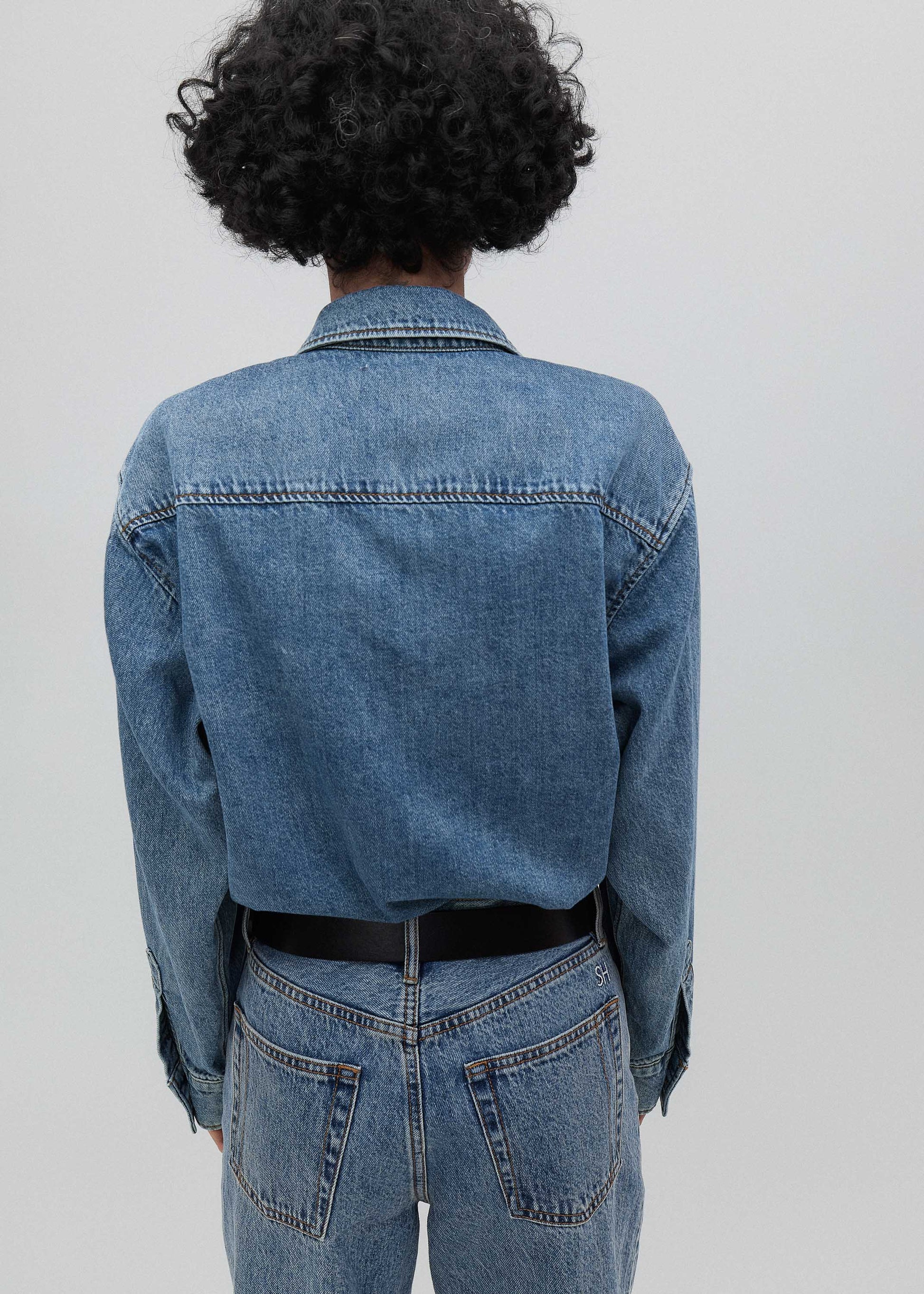 Person wearing a blue denim jacket and jeans from behind on a plain background