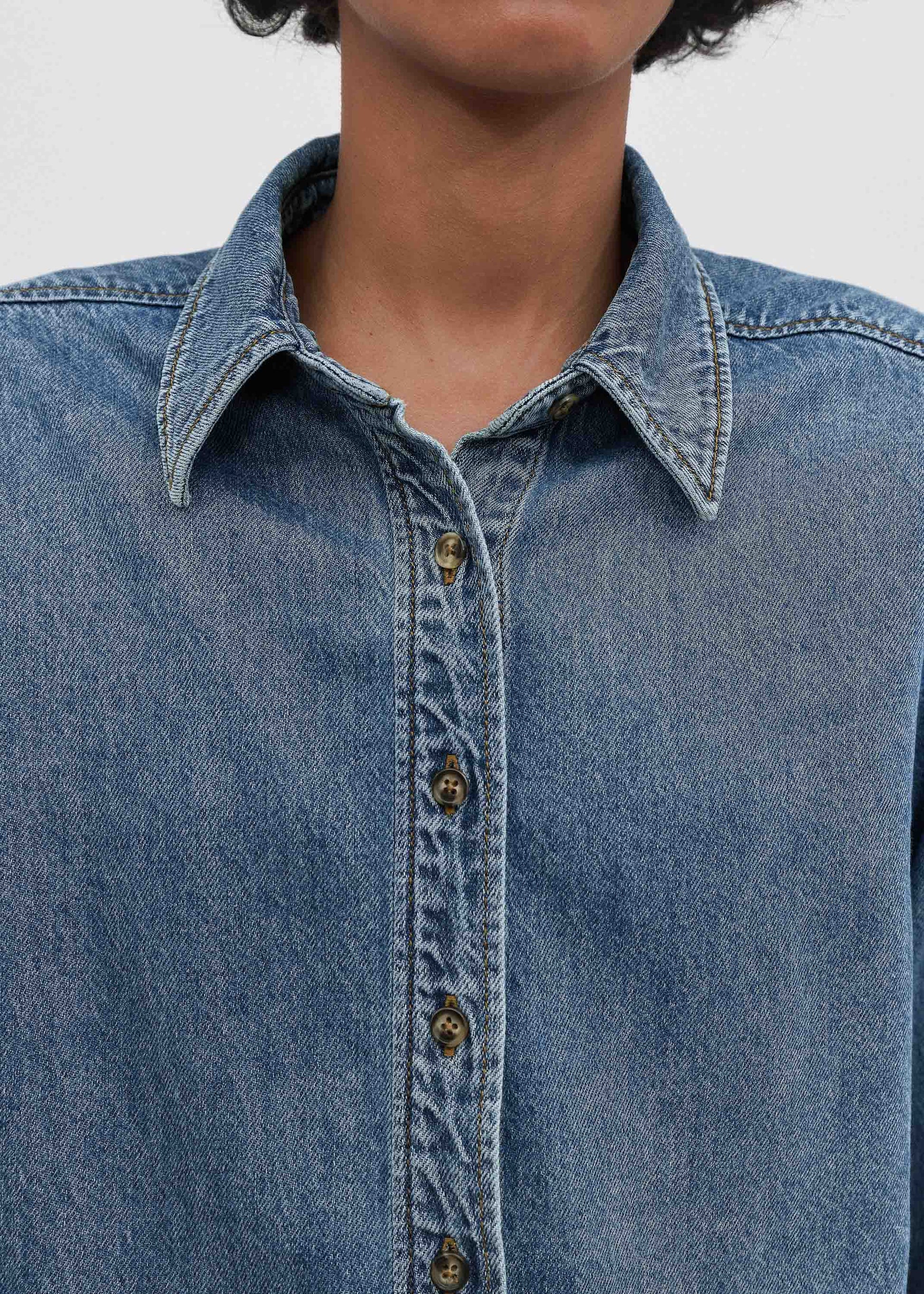 Close-up of a person wearing a blue denim shirt with a blurred background