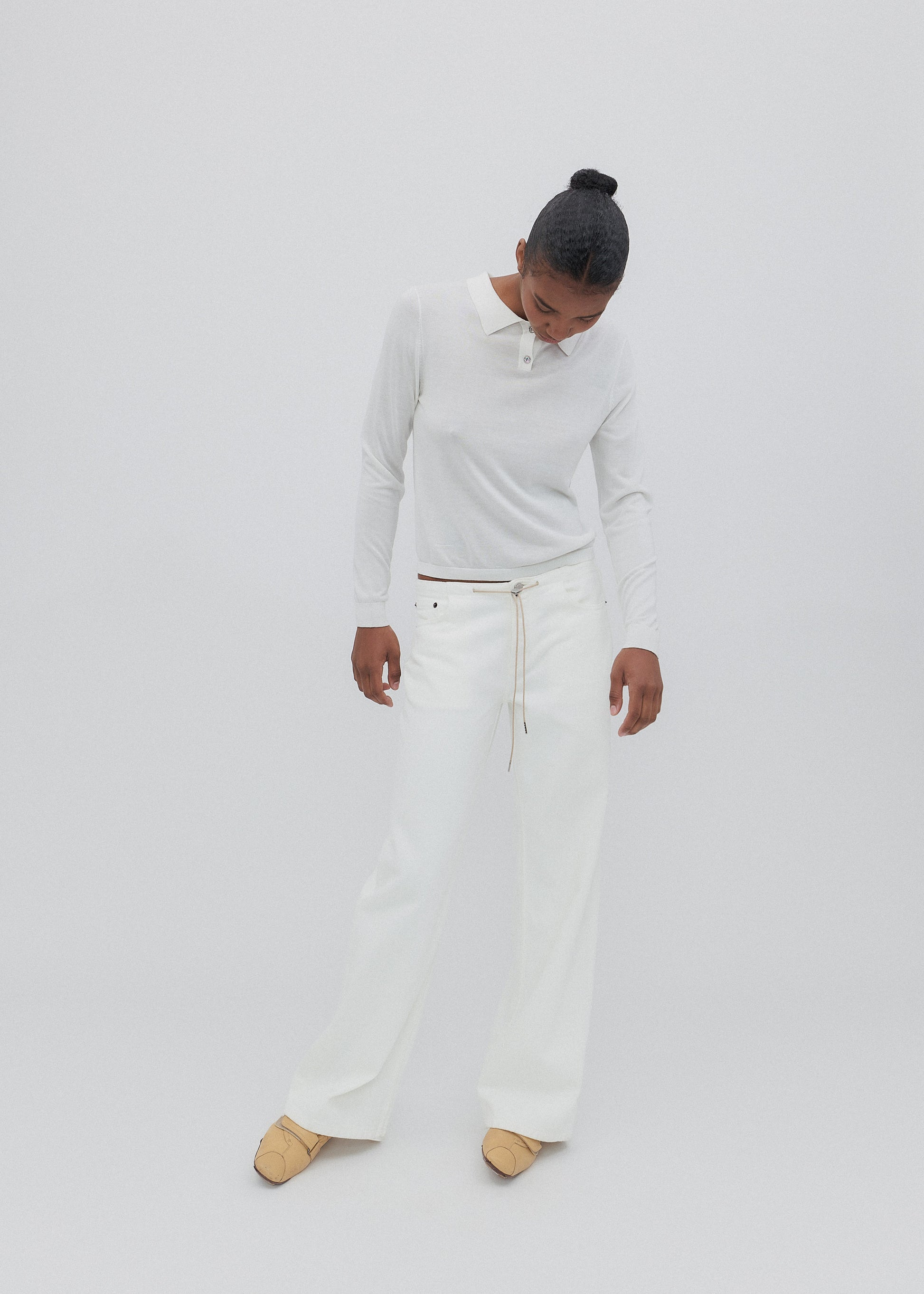 Person wearing a light gray sweater and white pants on a plain background