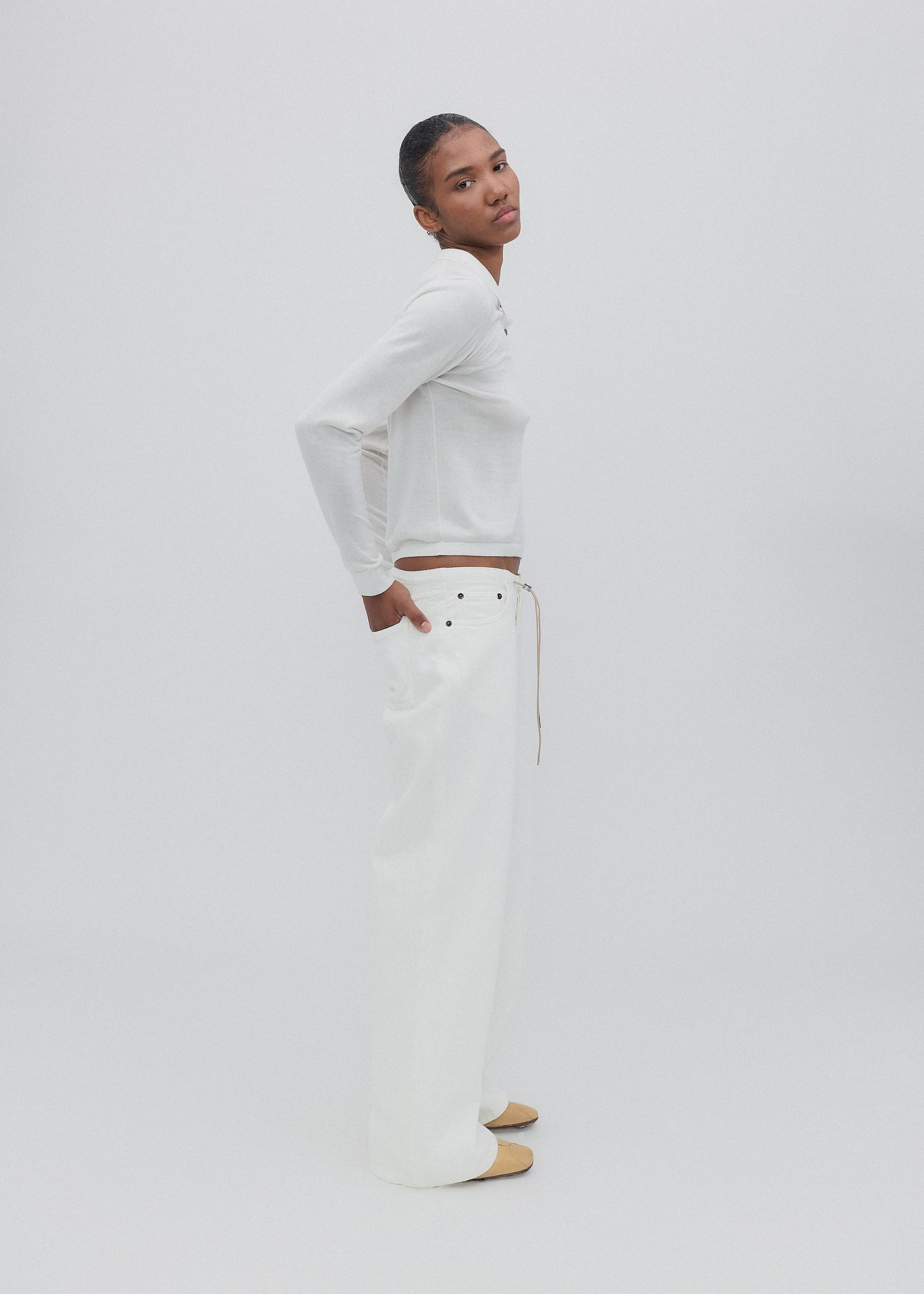 Person wearing a white long-sleeve top and light-colored pants on a plain background