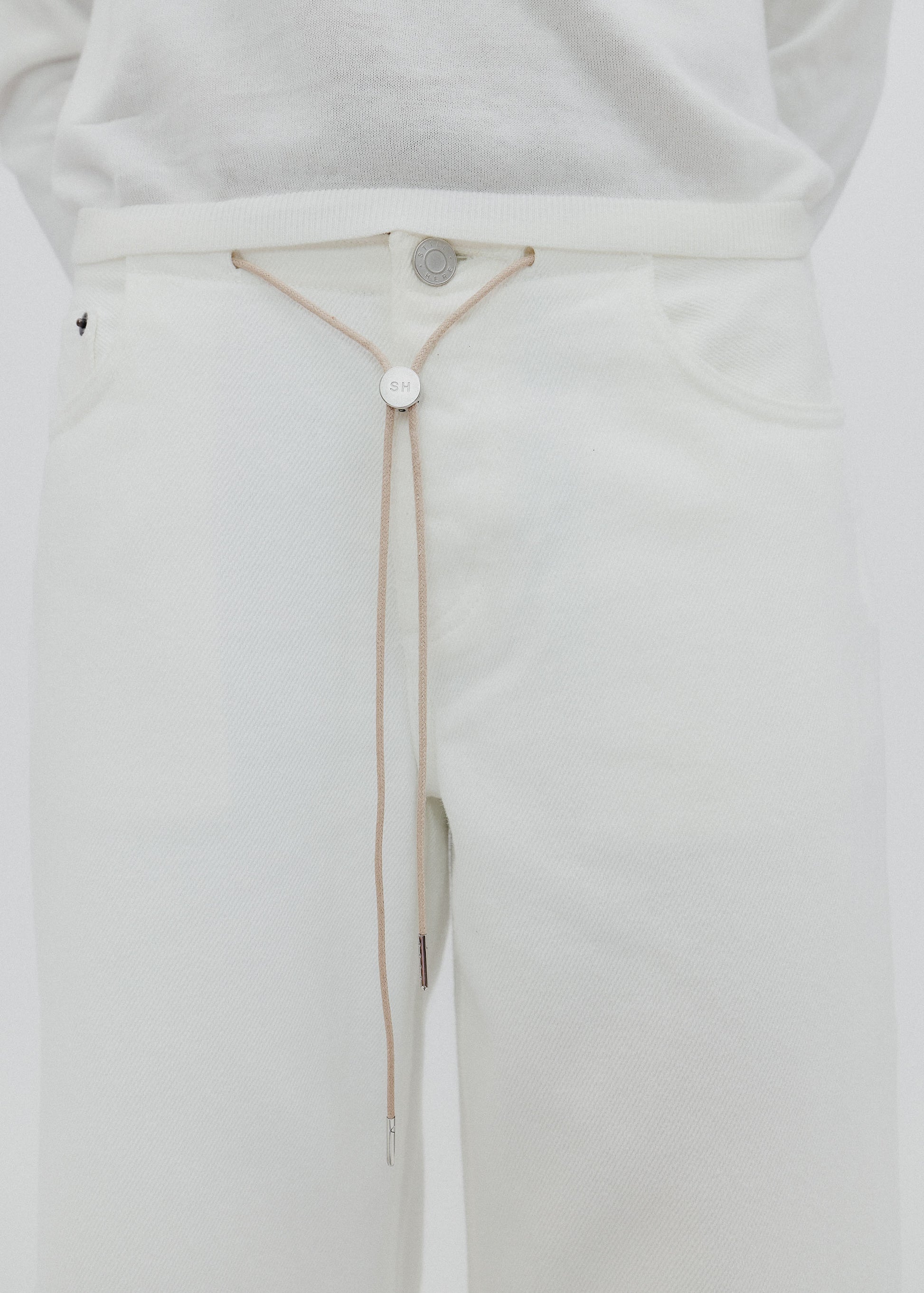 Close-up of a white garment with a thin strap and button detail on a light gray background