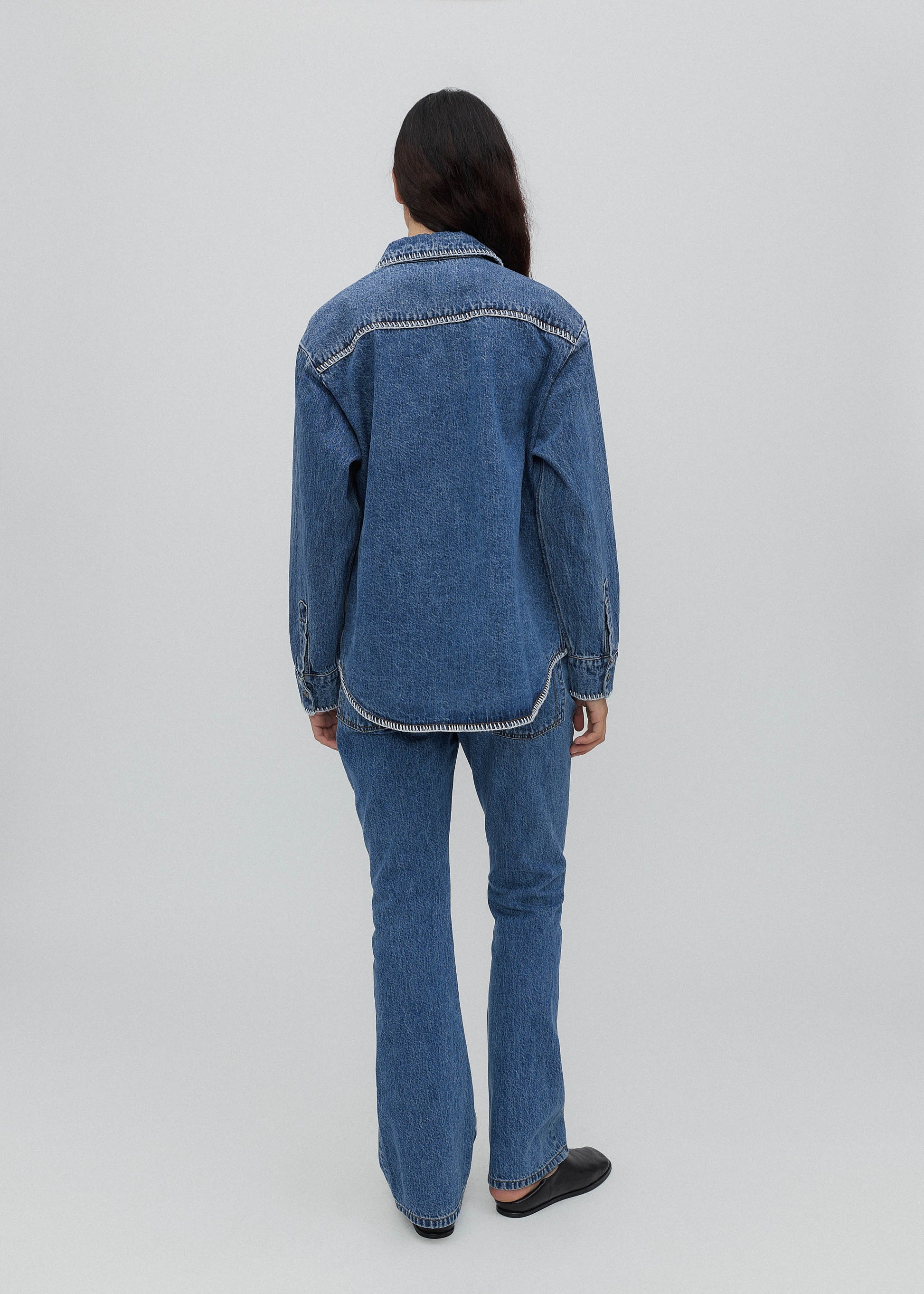 Person wearing a blue denim jacket and jeans on a white background