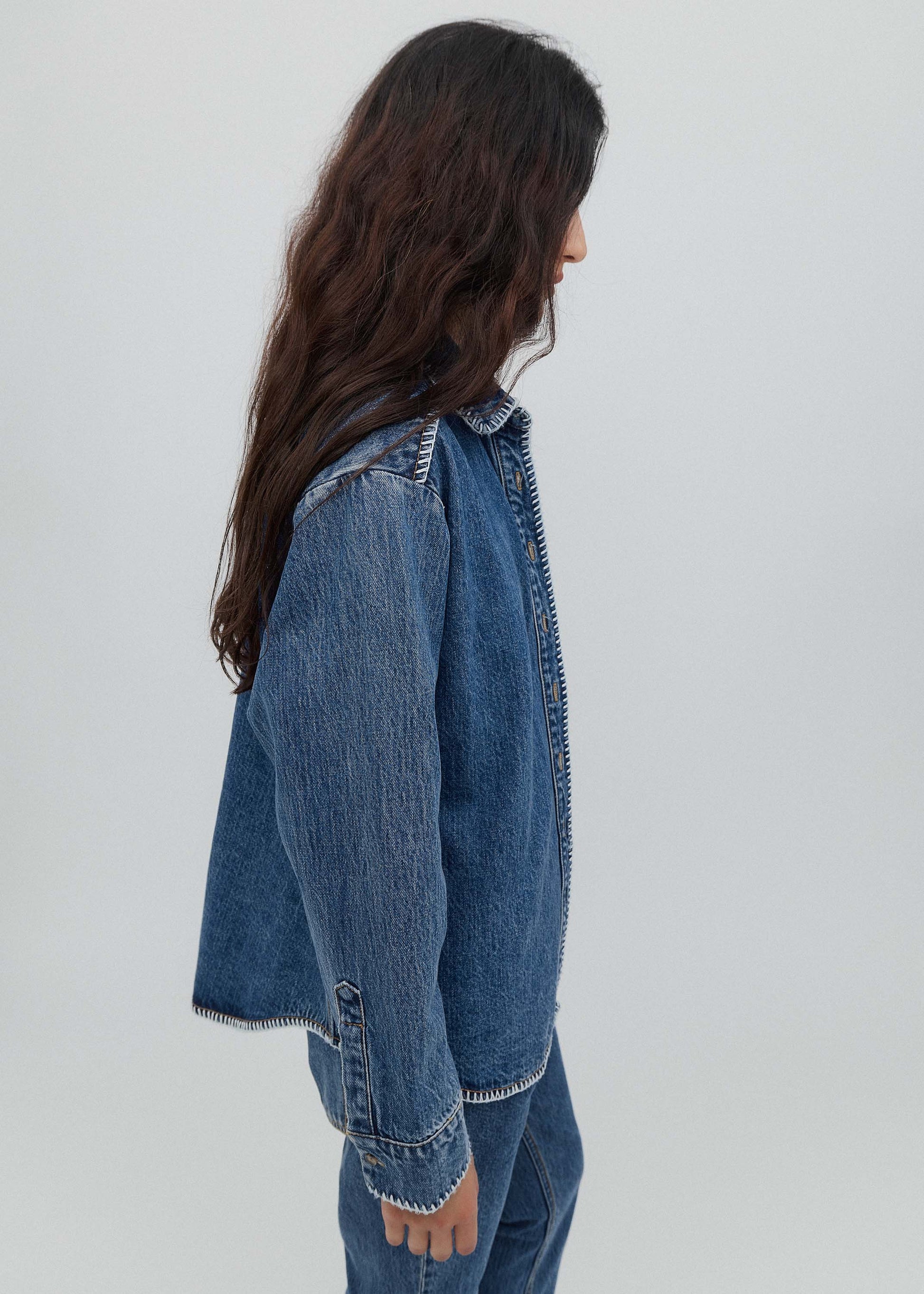Person wearing a blue denim jacket and jeans on a plain background