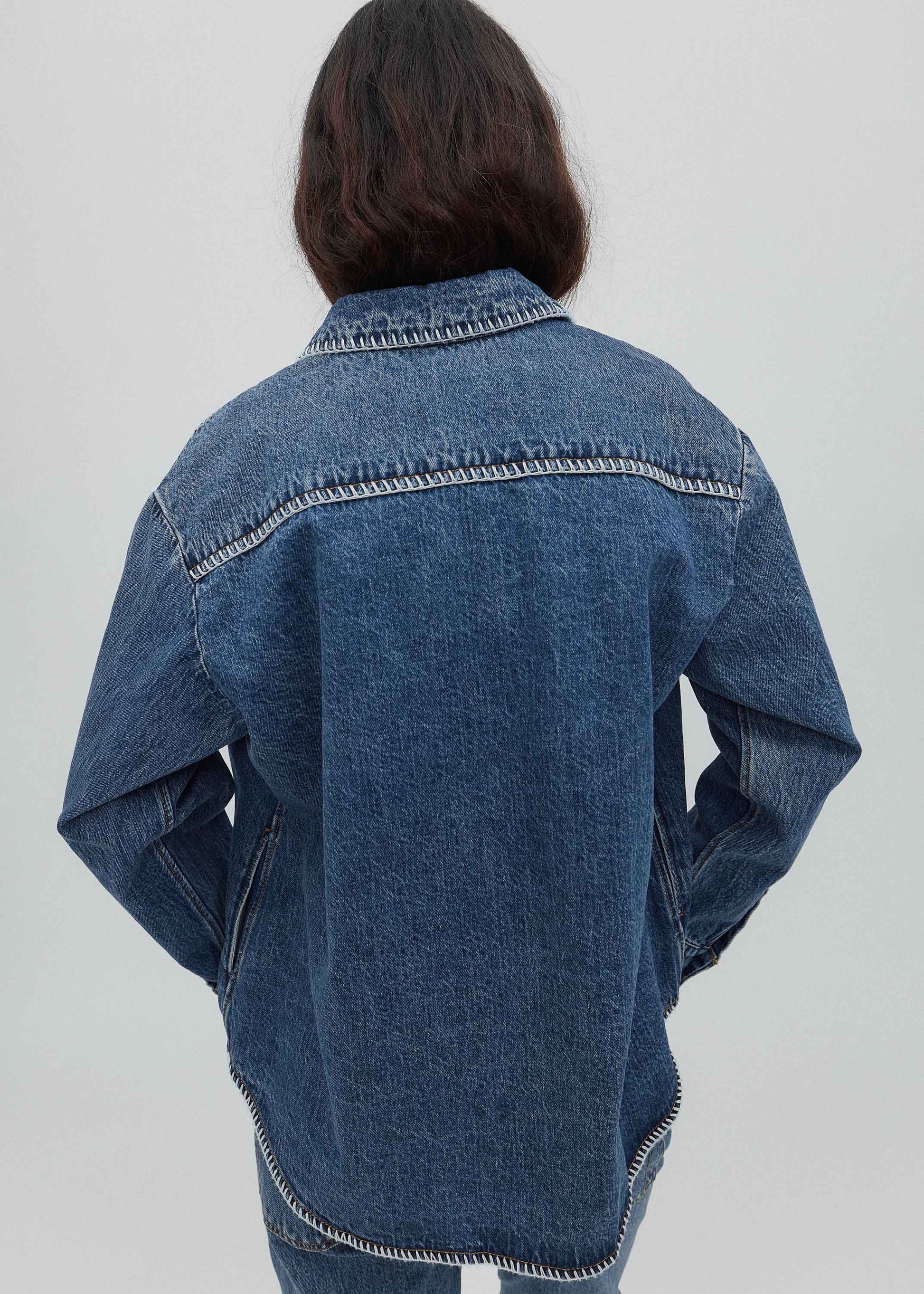 Person wearing a blue denim jacket on a plain background