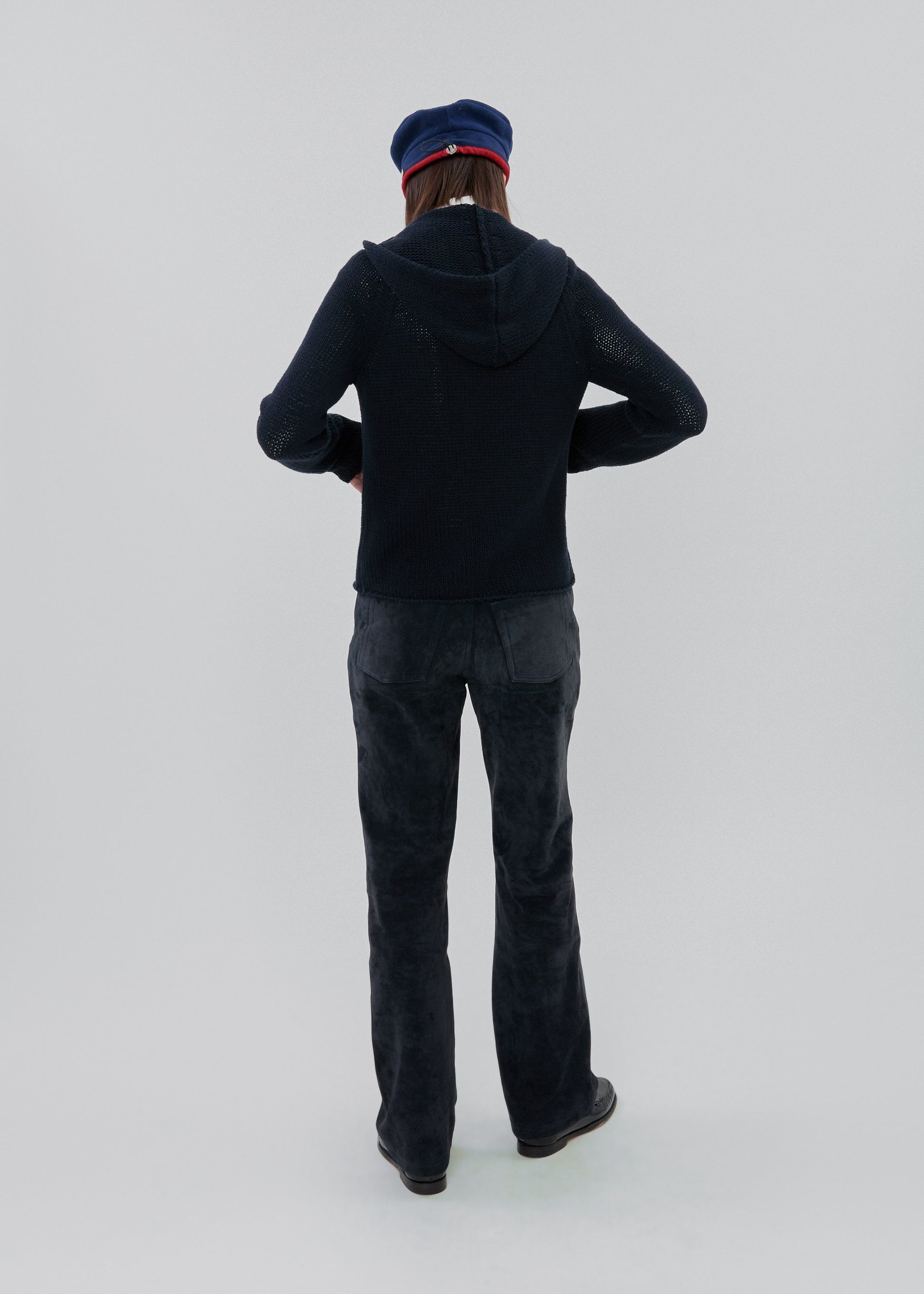 Person wearing a dark hoodie and jeans with a blue cap on a light gray background