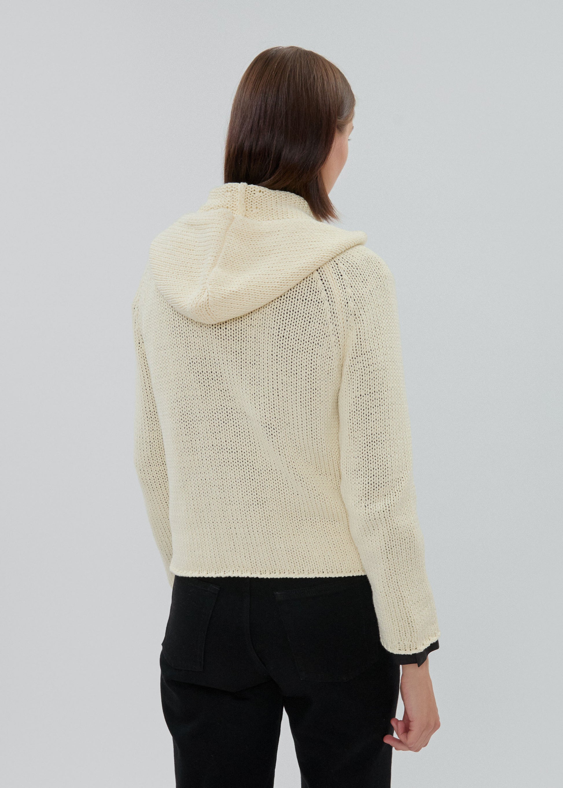 Person wearing a cream-colored knit hoodie on a plain background