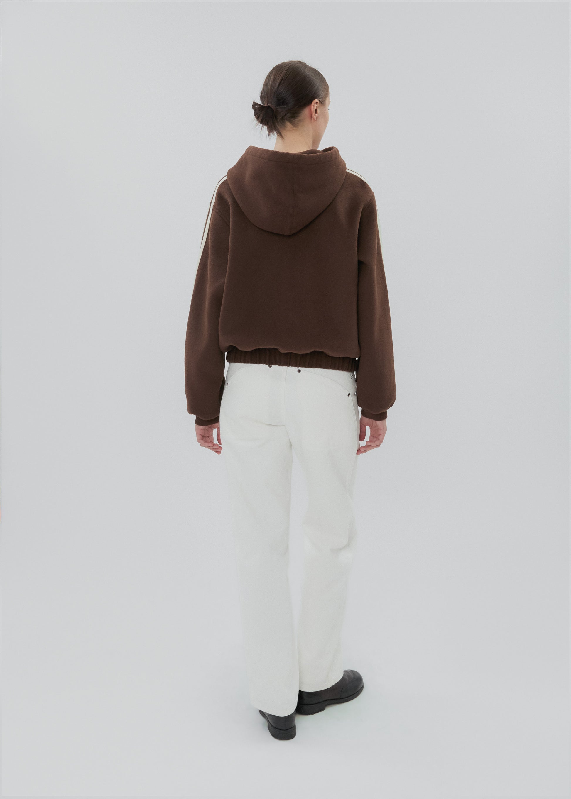 Person wearing a brown hoodie and white pants on a light gray background