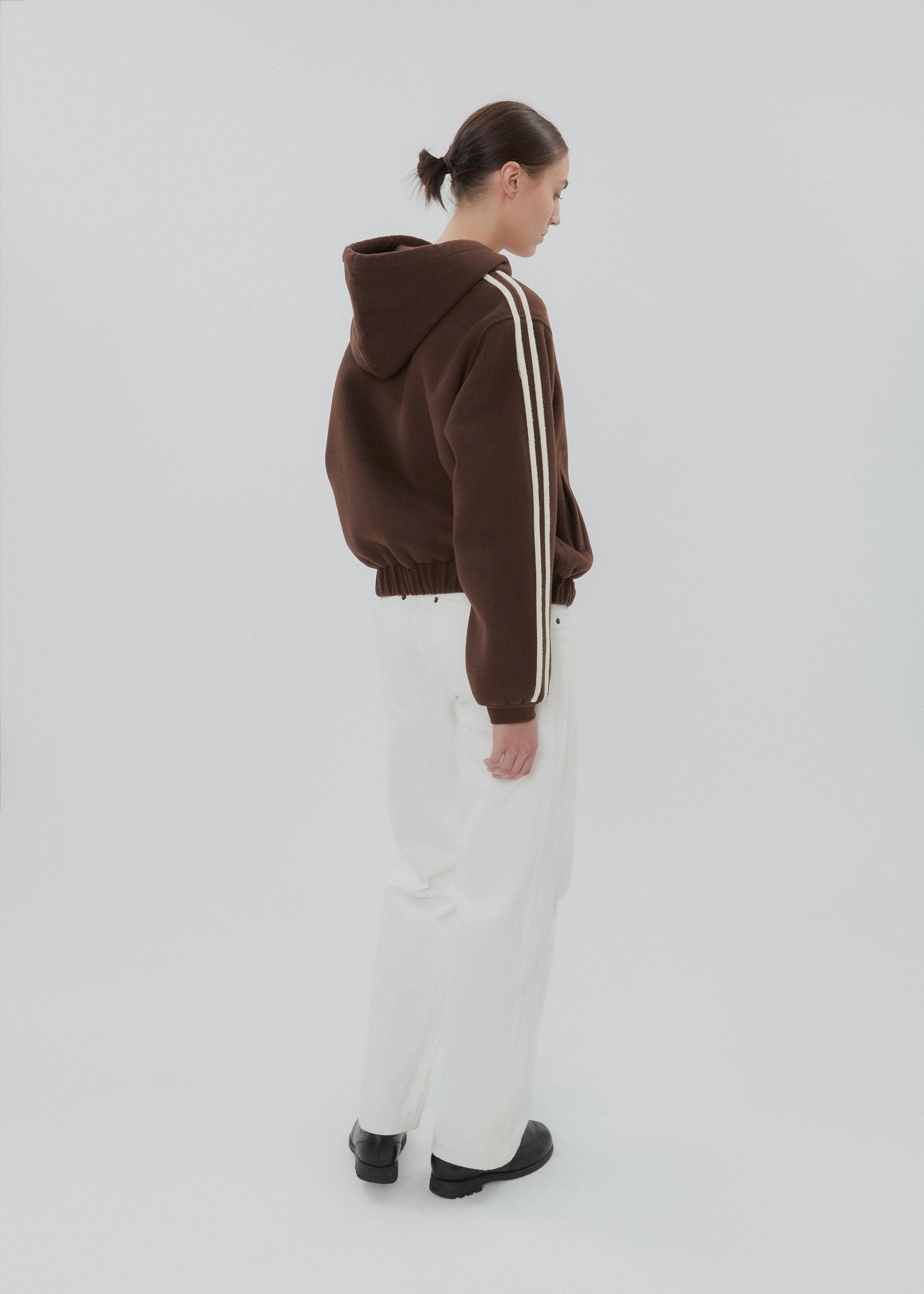 Person wearing a brown jacket with white stripes on a plain background