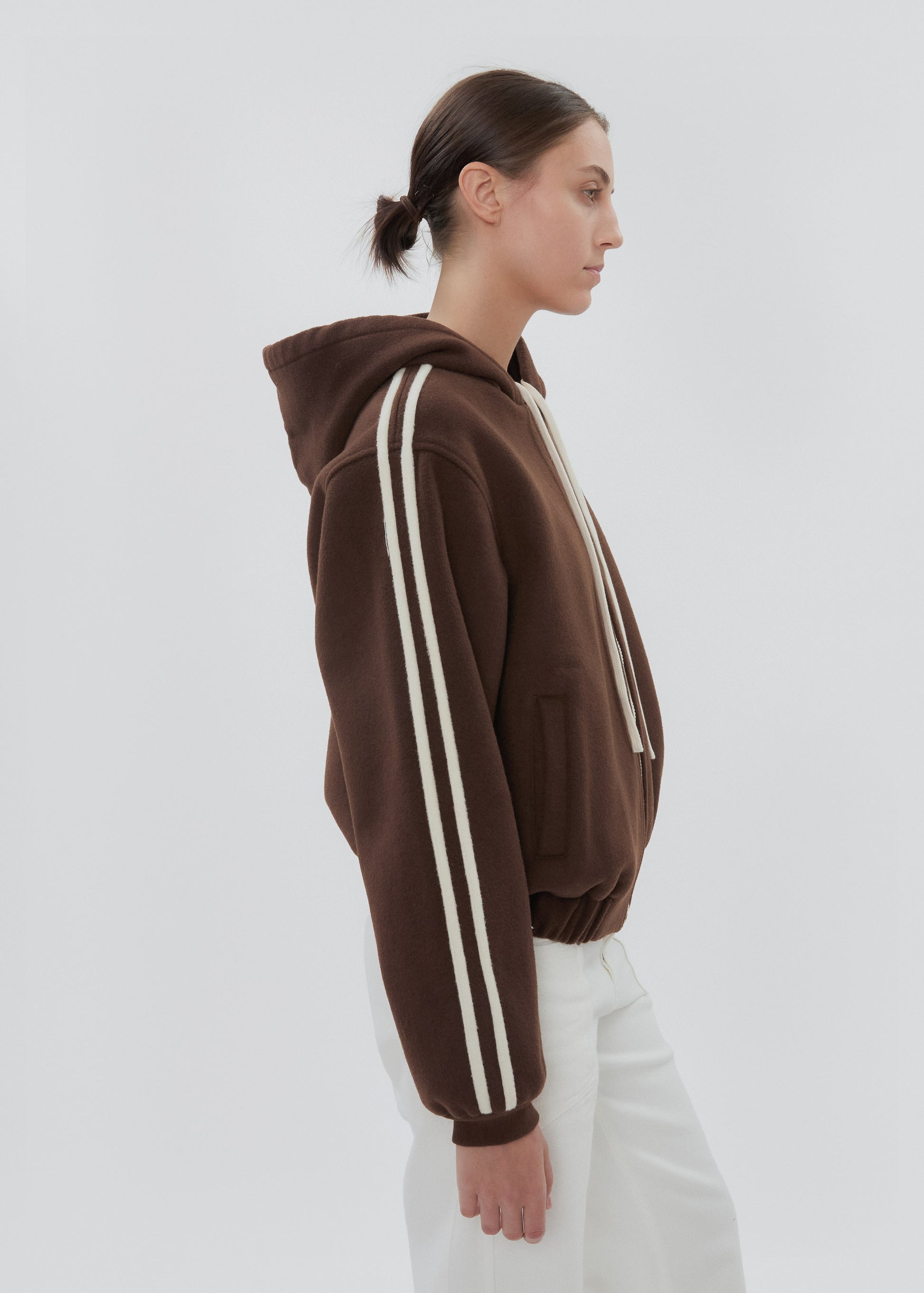 Person wearing a brown hoodie with white stripes on a plain background