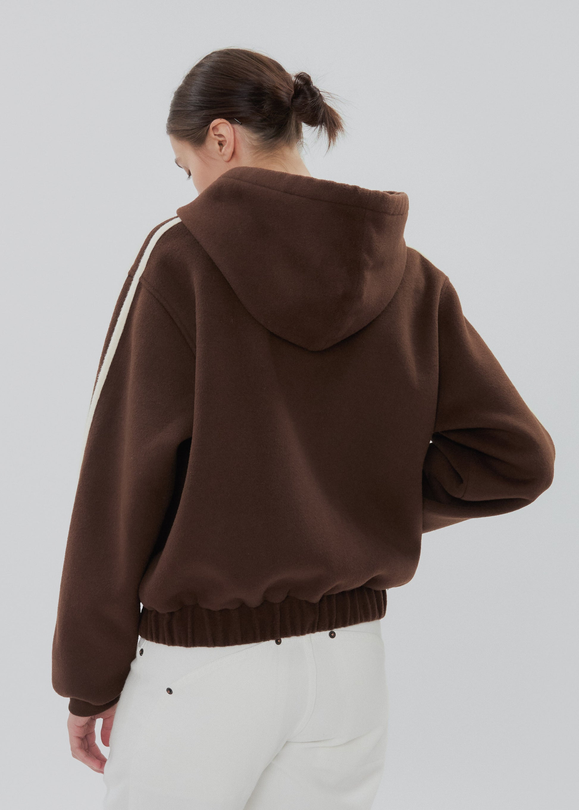 Person wearing a brown hoodie with a white stripe on a plain background