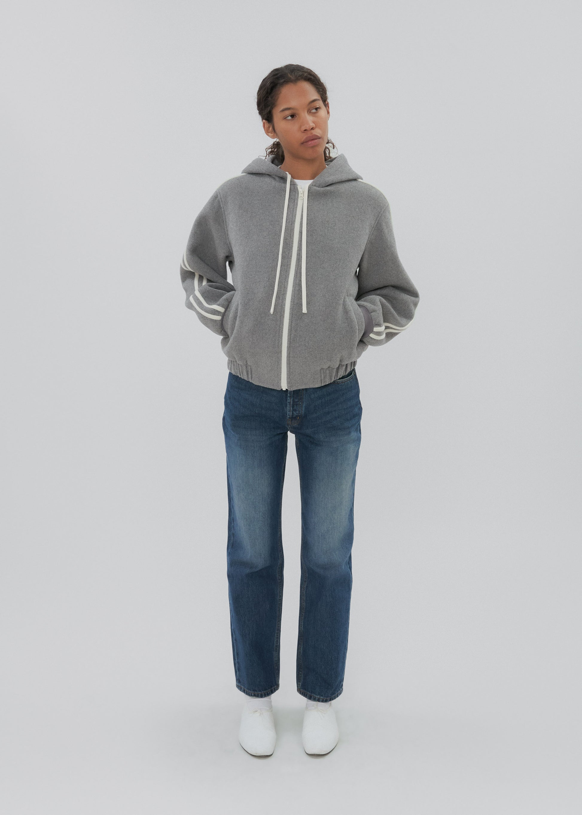 Person wearing a gray hoodie and blue jeans on a white background