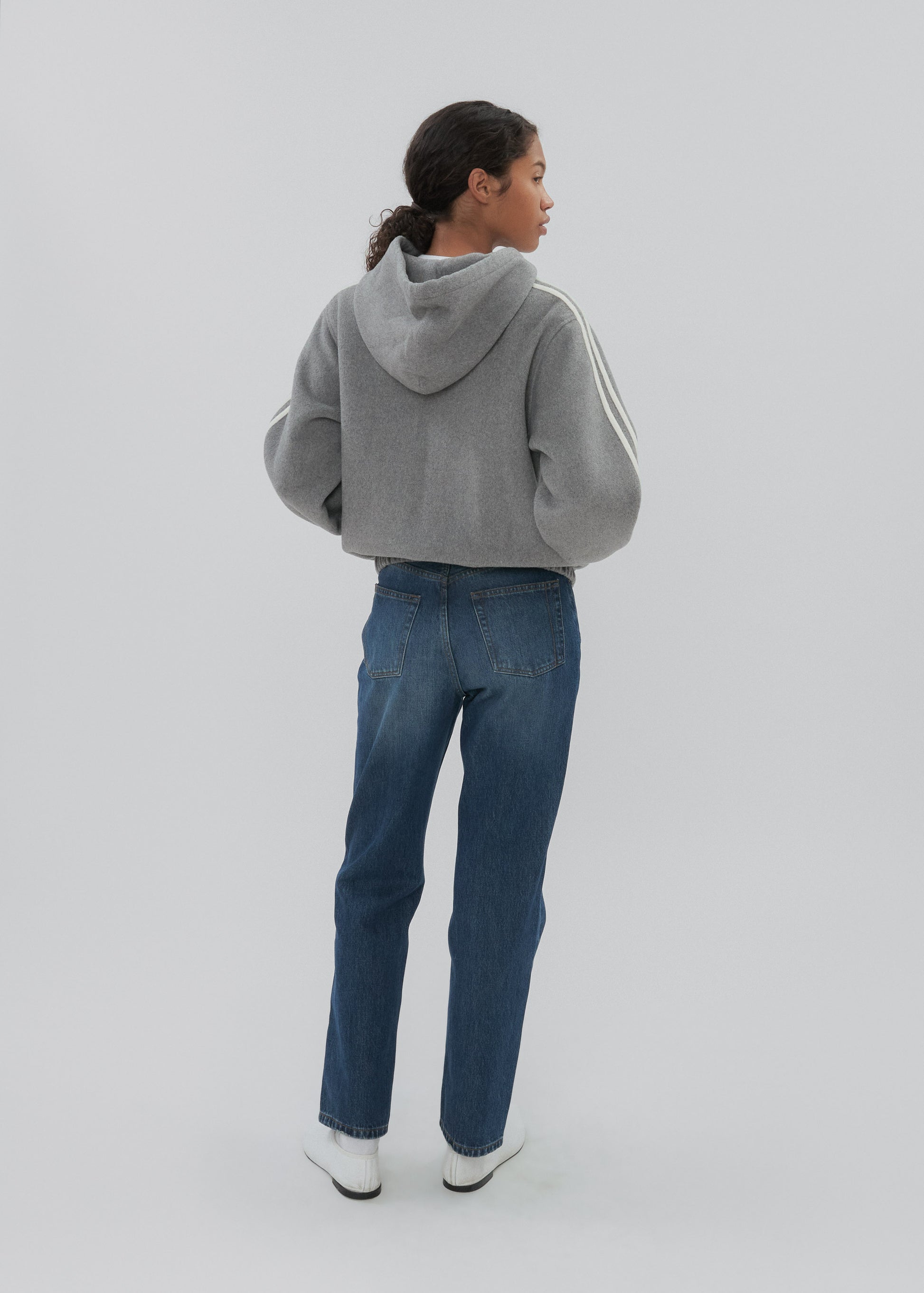 Person wearing a gray hoodie and blue jeans on a white background