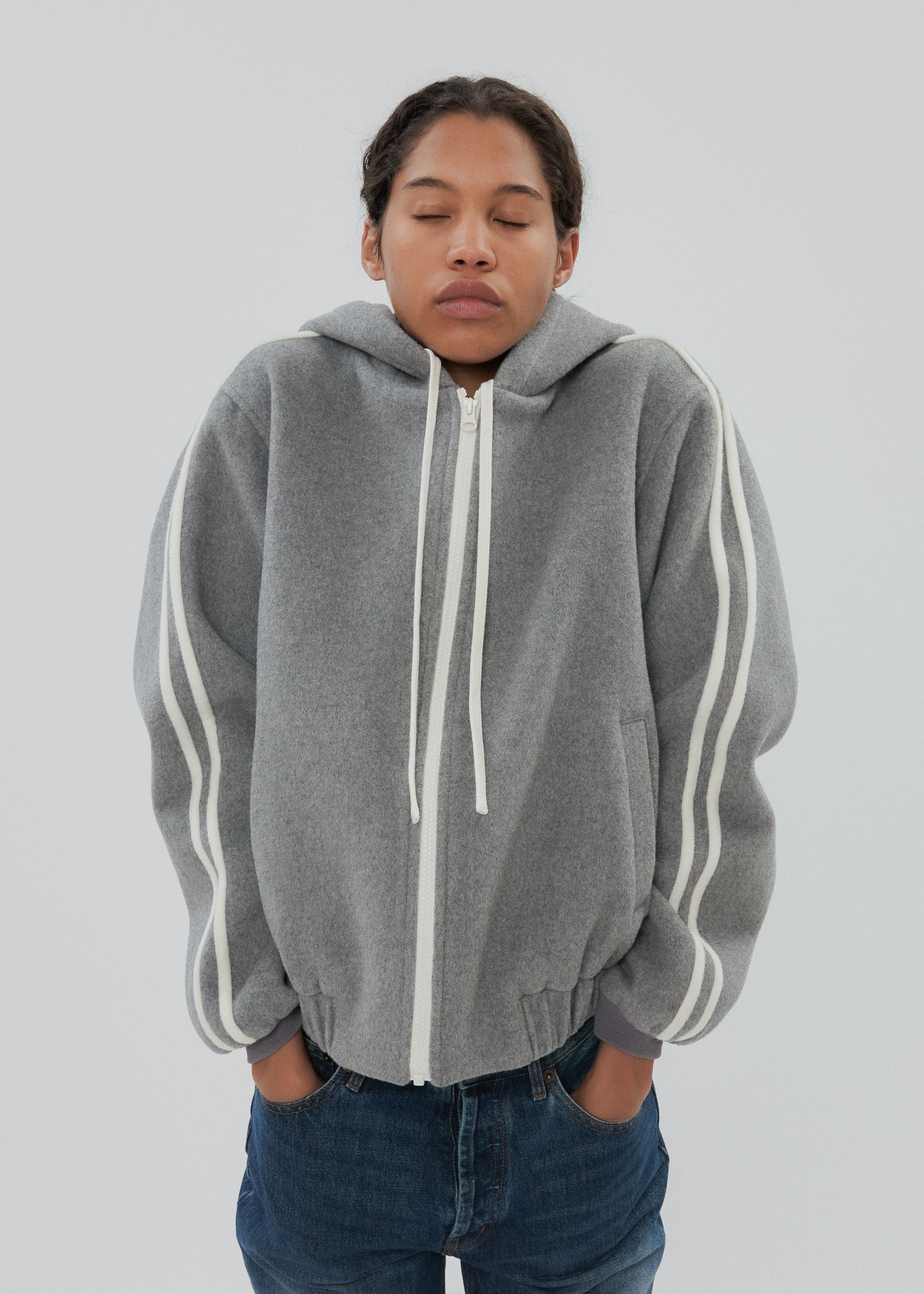Person wearing a gray hoodie with white stripes on a plain background