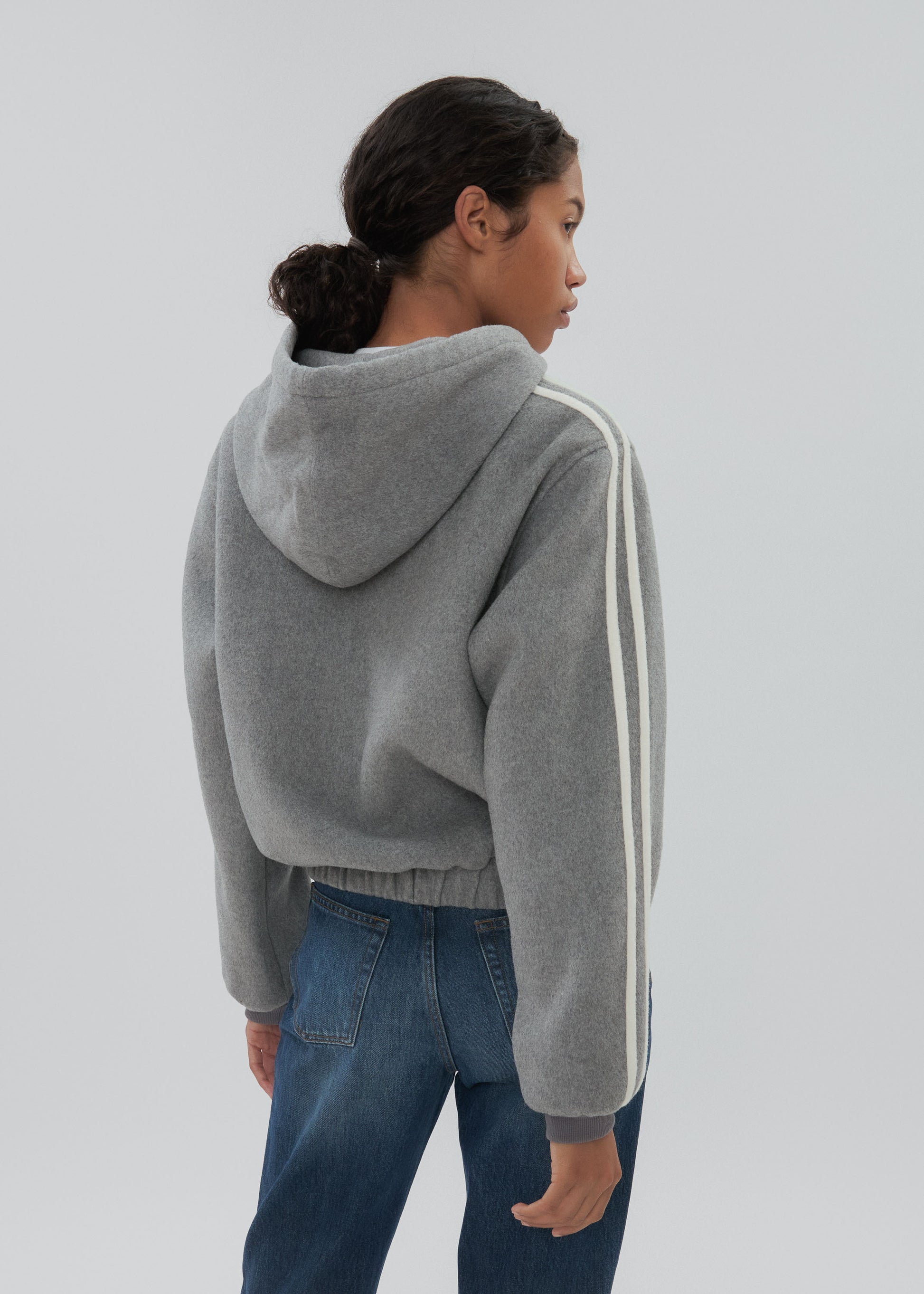 Person wearing a gray hoodie with white stripes on a plain background
