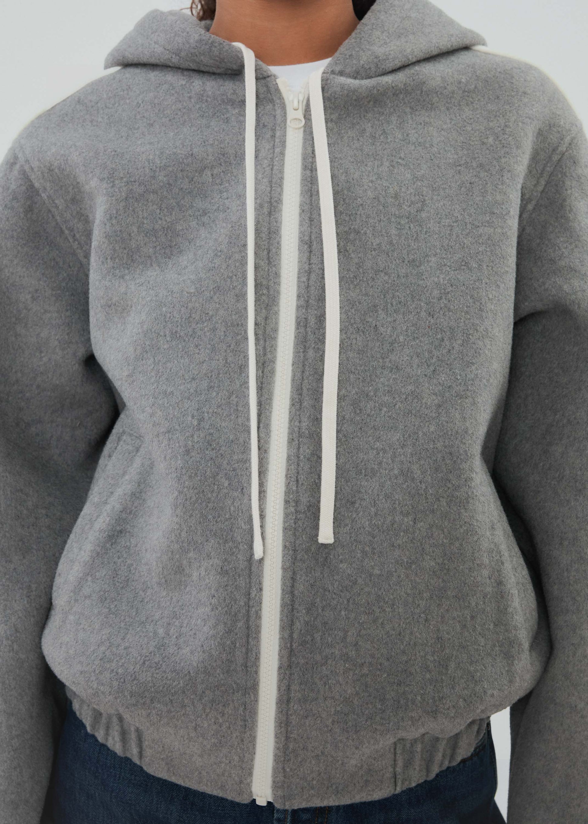 Gray hoodie with a white zipper on a neutral background