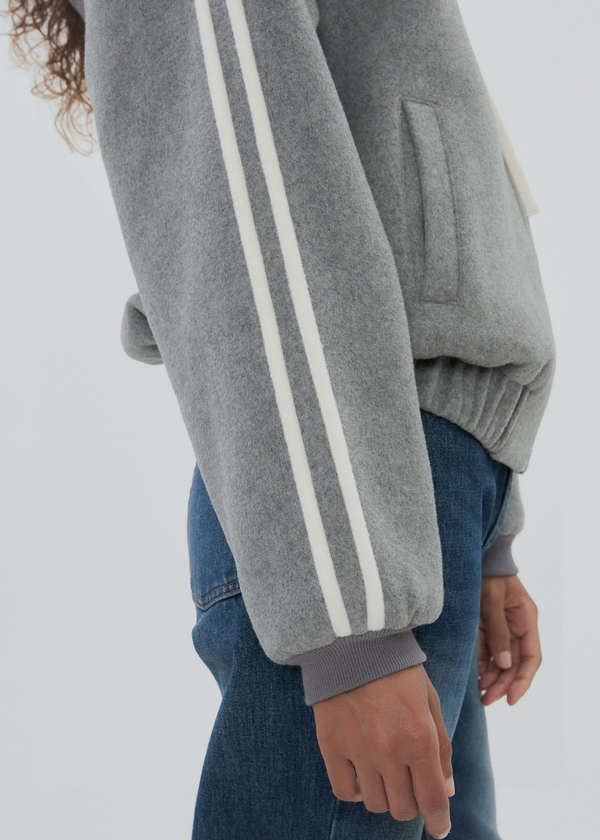 Gray sweatshirt with white stripes on sleeves and blue jeans against a light gray background