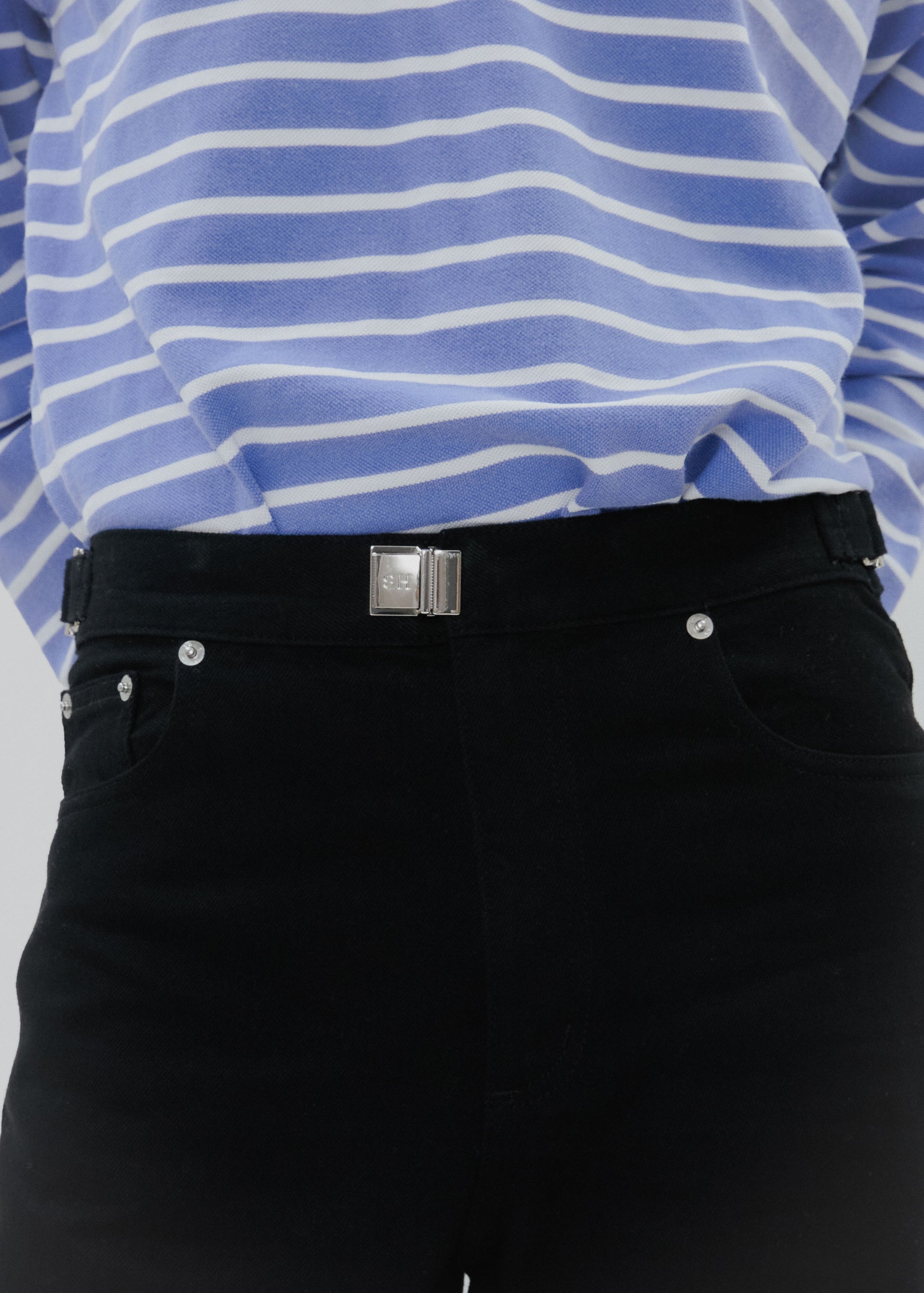 Close-up of a person wearing a blue and white striped shirt with black pants on a light gray background