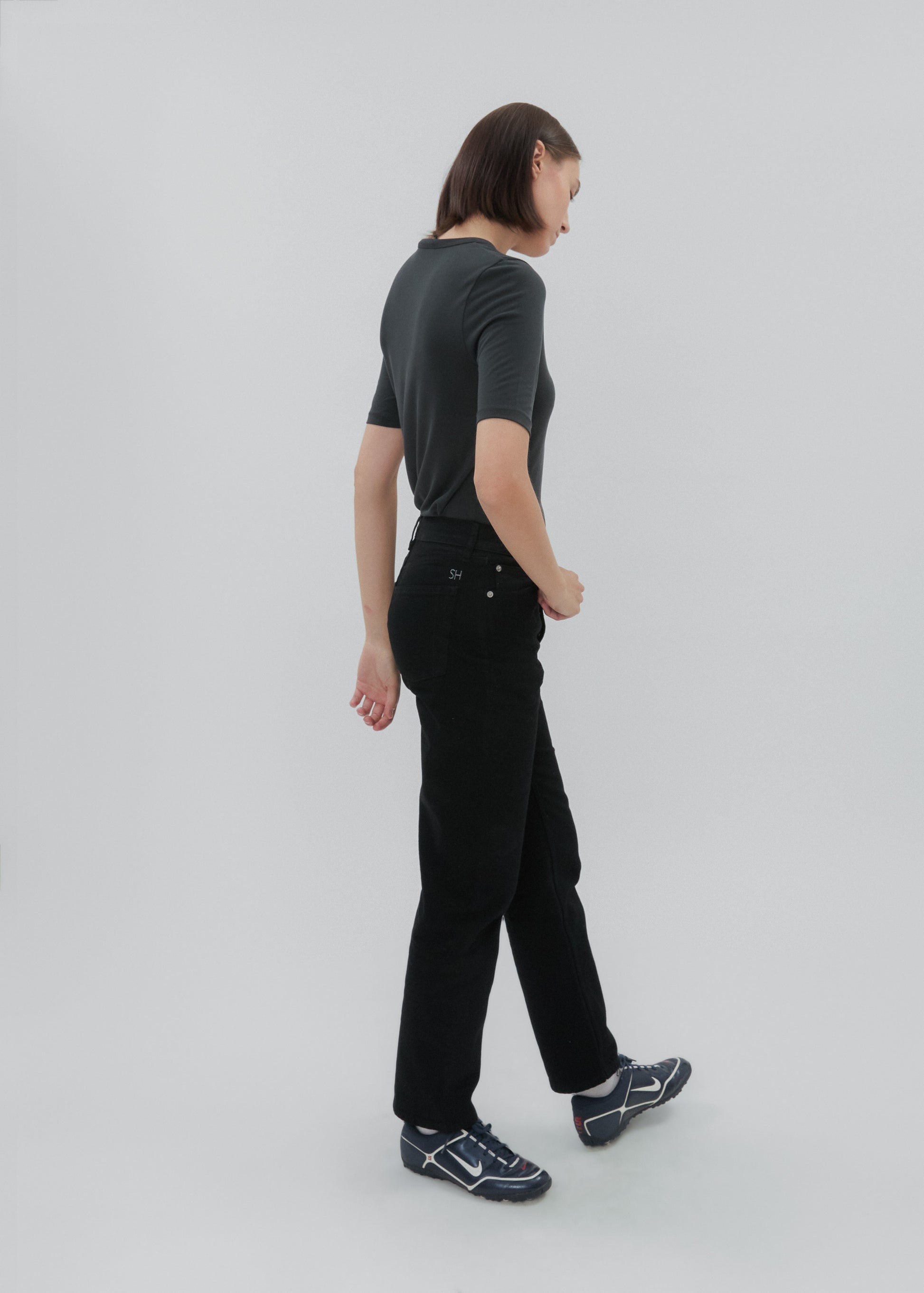 Person wearing a dark green t-shirt and black pants on a light gray background