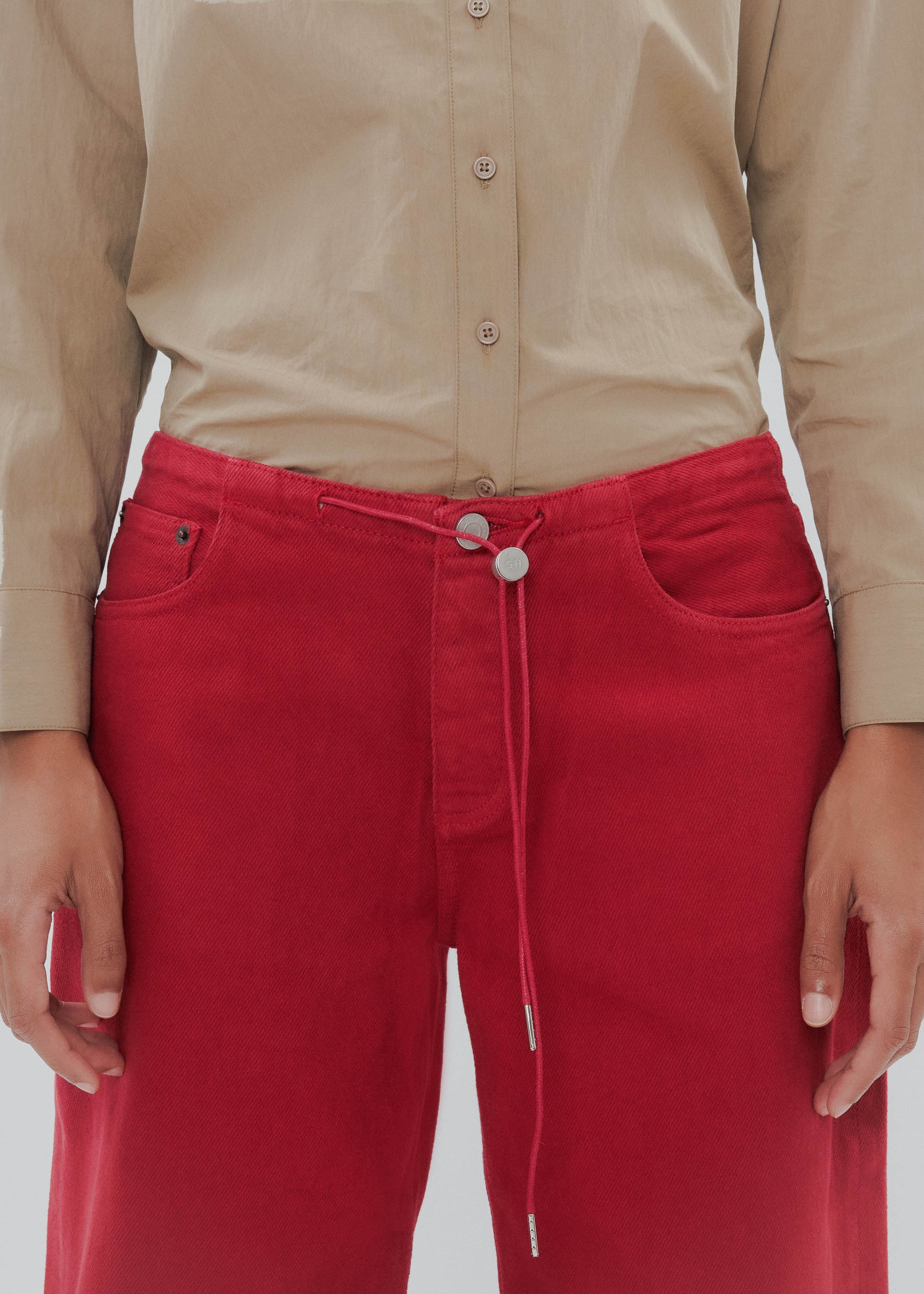 Person wearing a beige shirt and red pants on a plain background