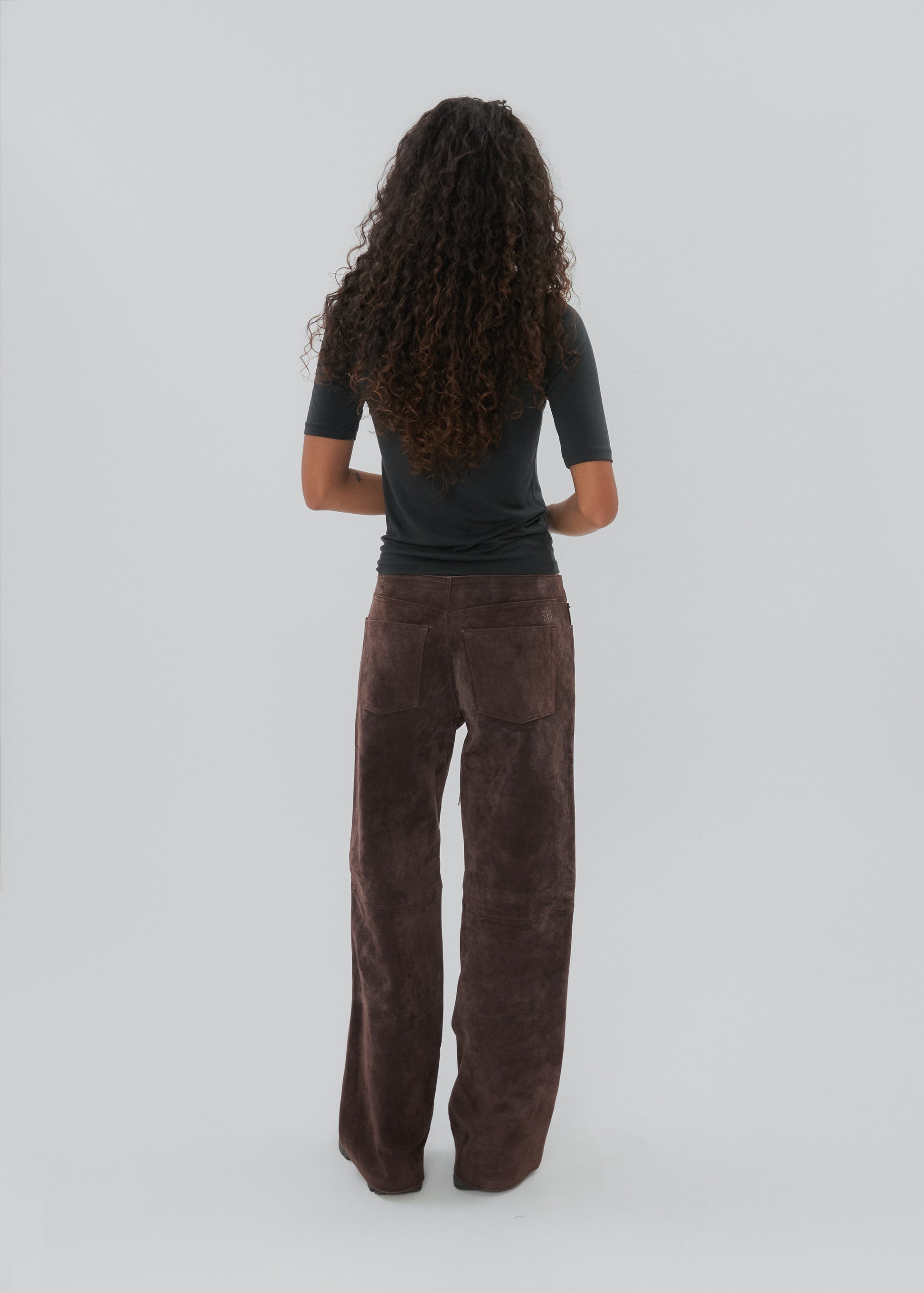 Person wearing a black top and brown pants on a white background