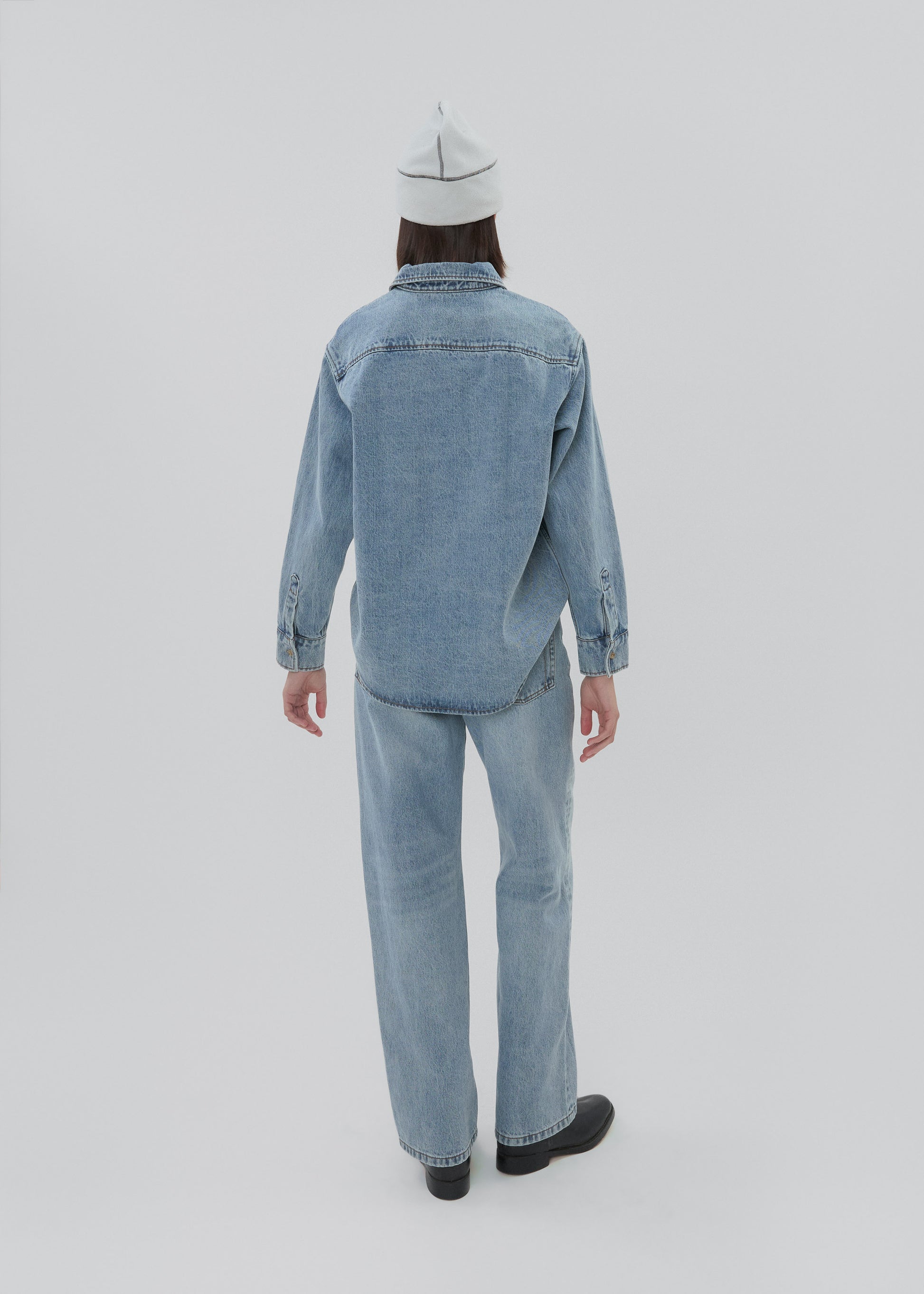 Person wearing a light blue denim outfit on a white background