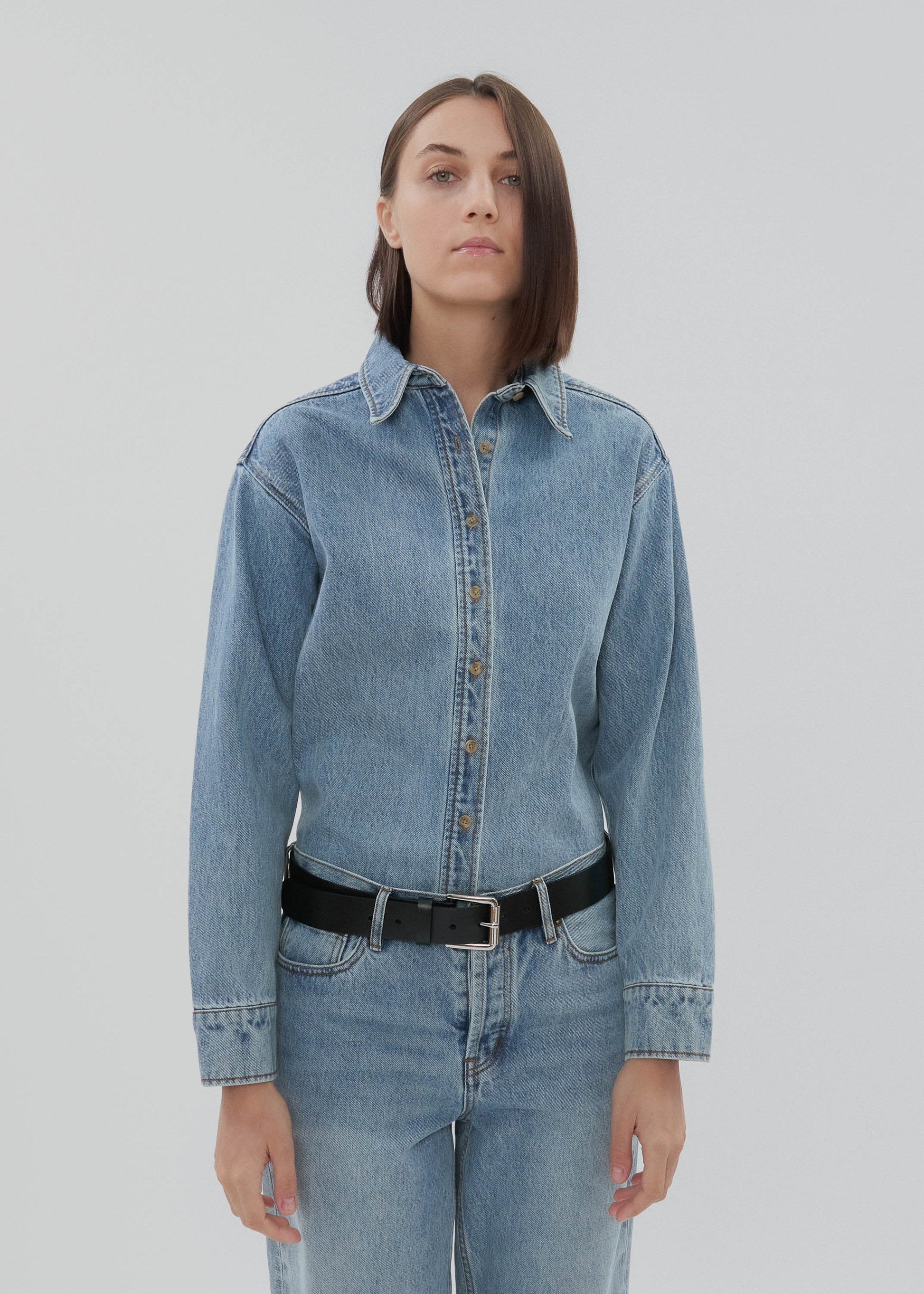 Person wearing a blue denim shirt and jeans on a plain background
