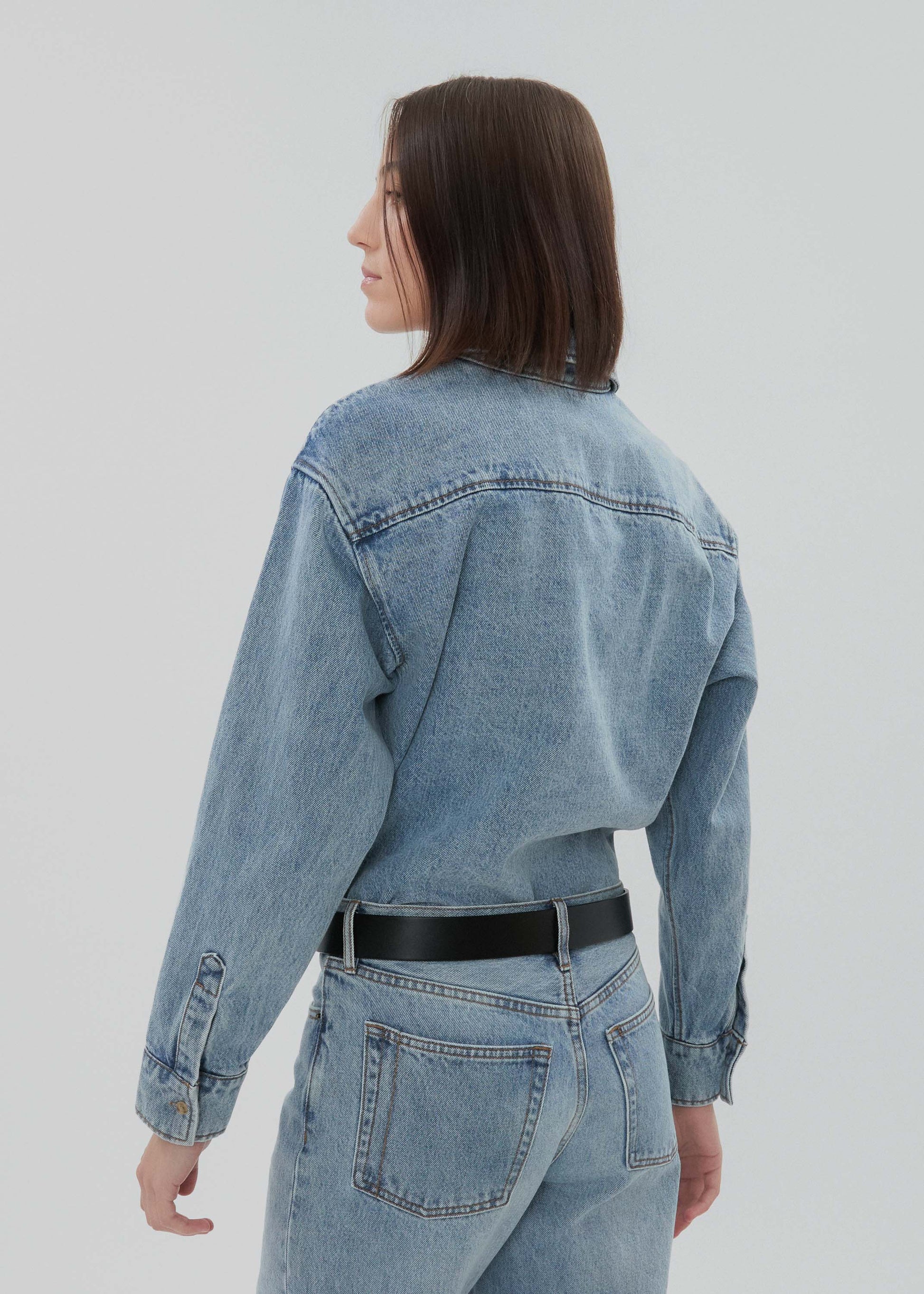 Person wearing a light blue denim jacket and jeans on a plain background