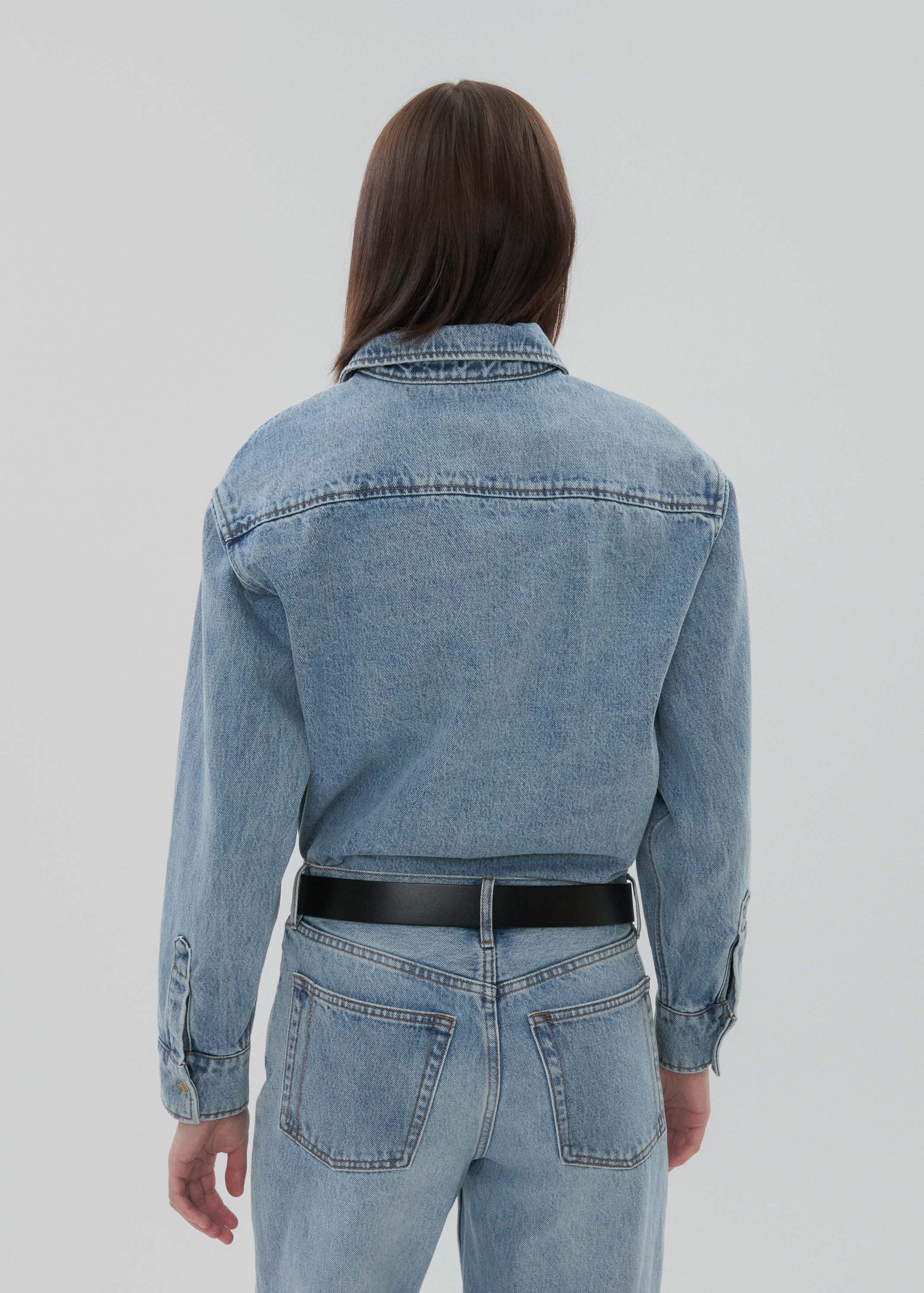 Person wearing a blue denim jacket and jeans on a plain background