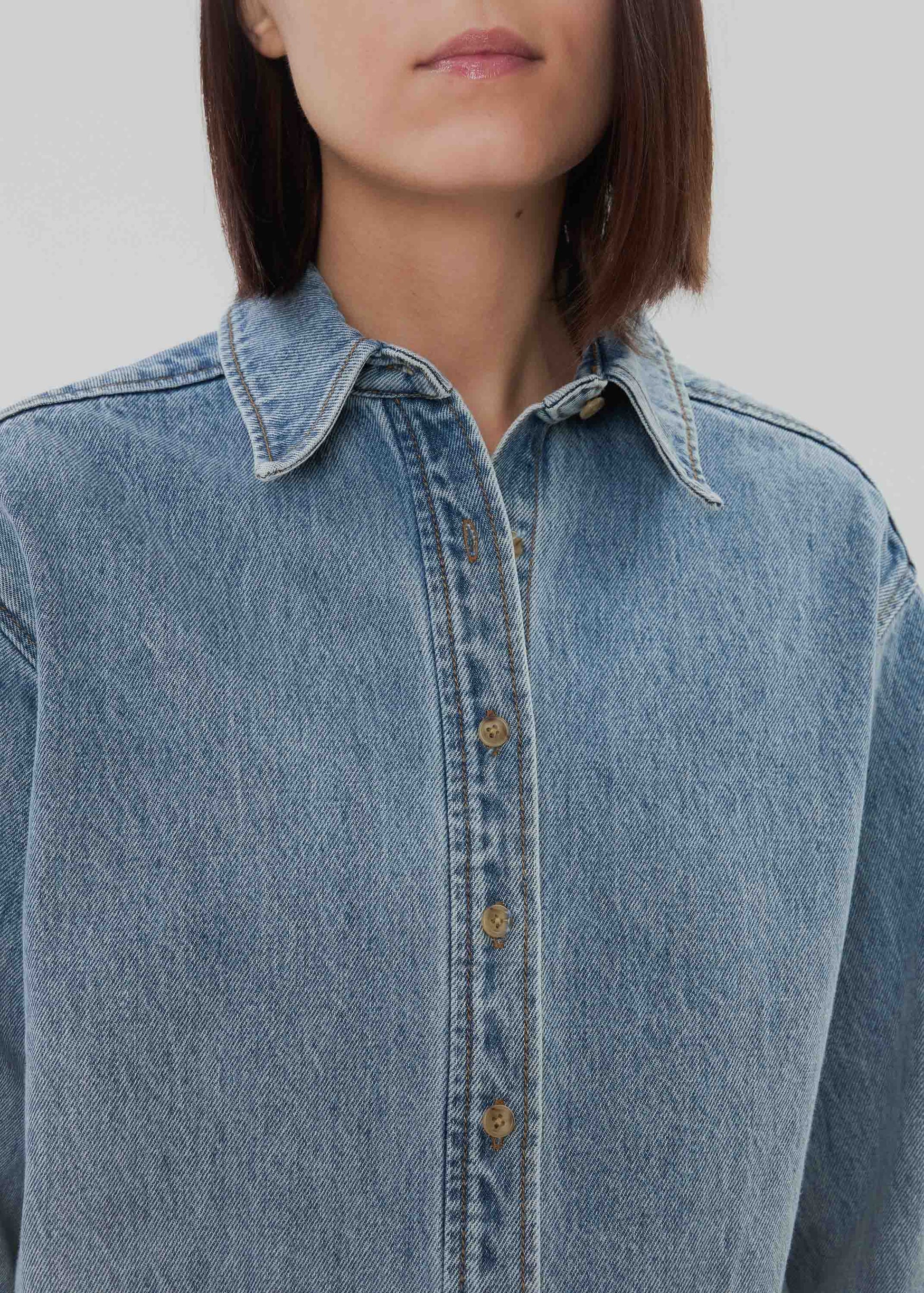 Close-up of a person wearing a light blue denim shirt against a neutral background