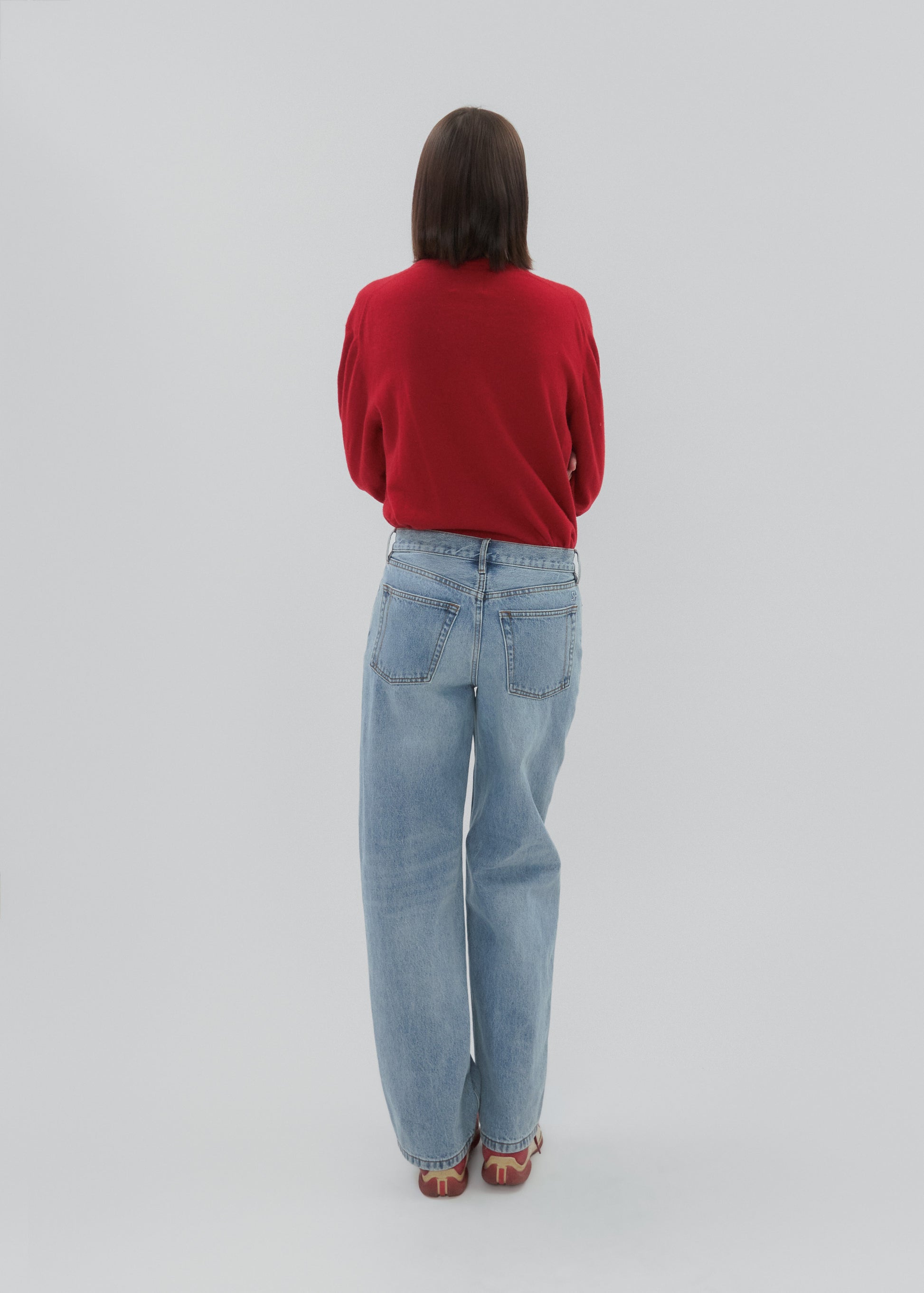Person wearing a red sweater and light blue jeans on a plain background