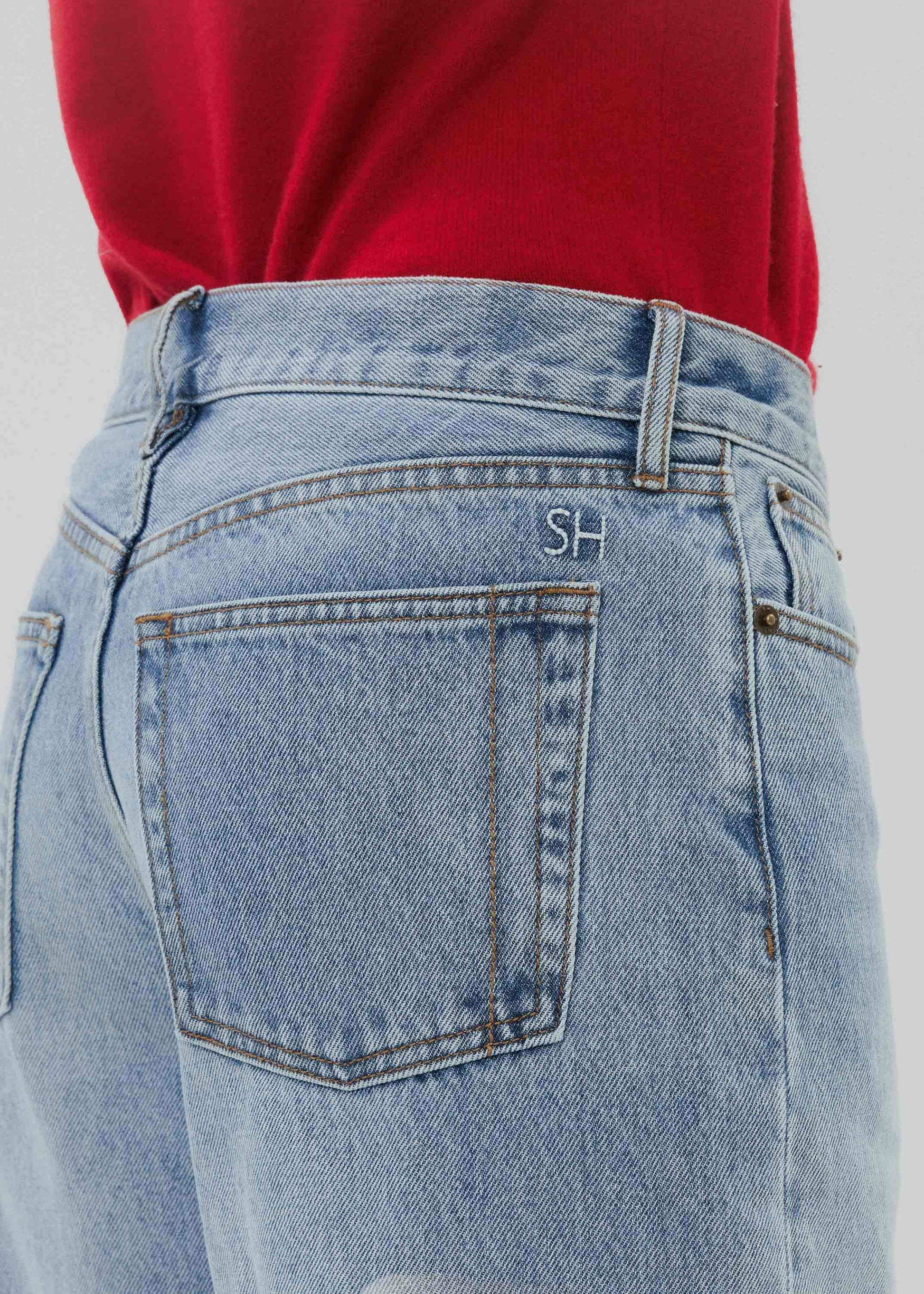 Close-up of light blue jeans with a red shirt worn underneath on a plain background