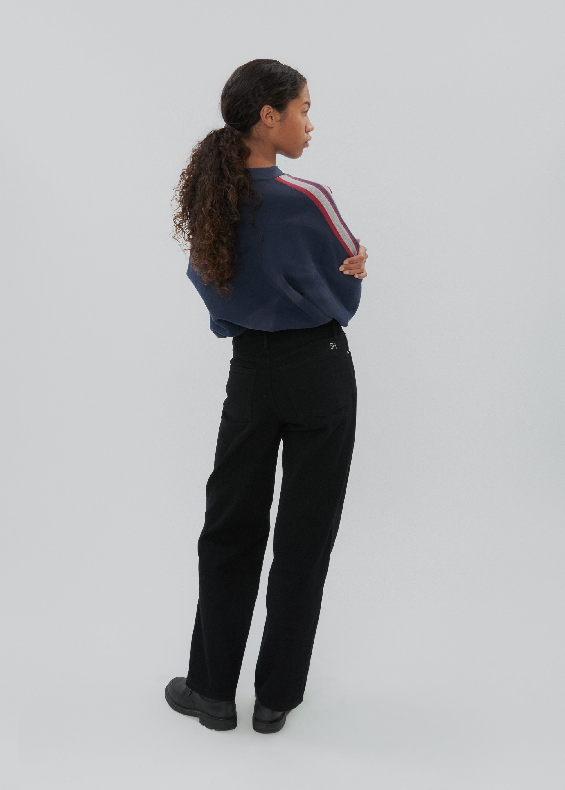 Person wearing a navy sweater with red and white stripes and black pants on a light gray background