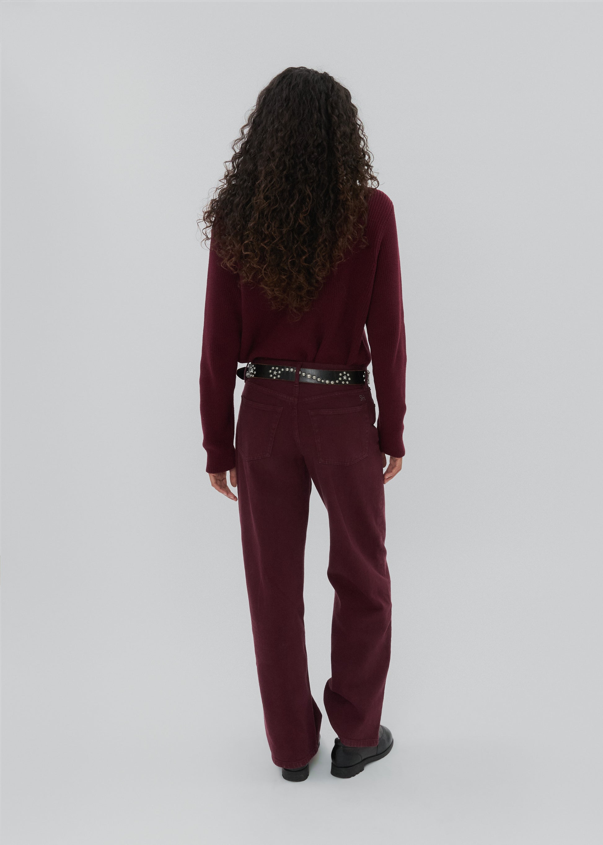 Person wearing a burgundy outfit with a belt on a white background