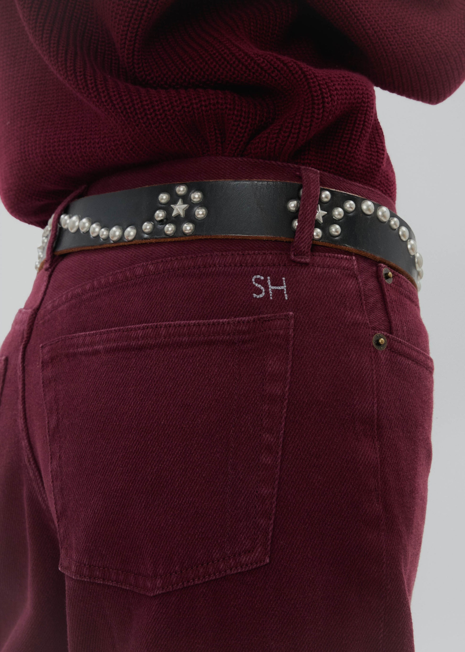Maroon pants with a studded belt on a plain background