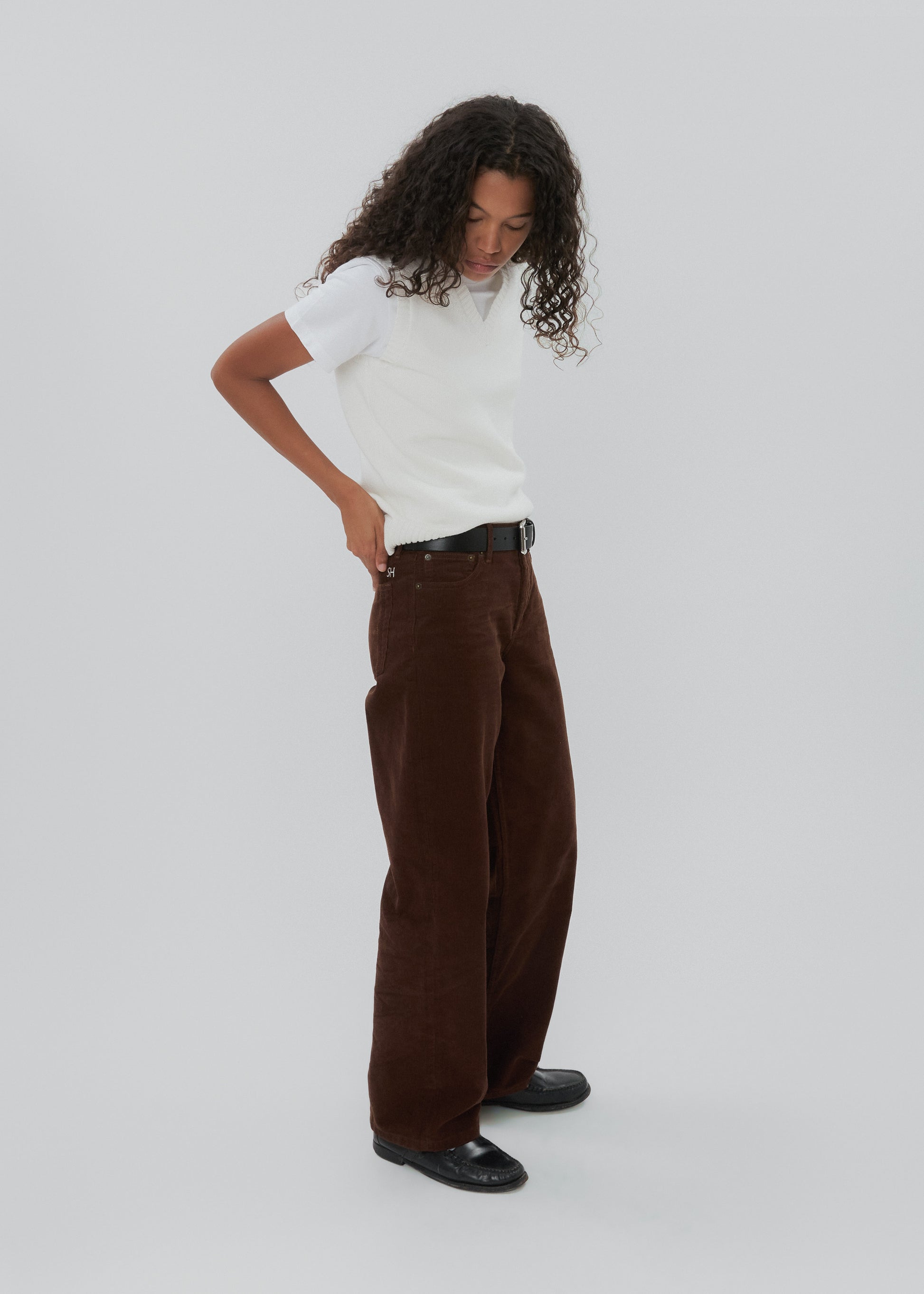 Person wearing a white shirt and brown pants on a plain background