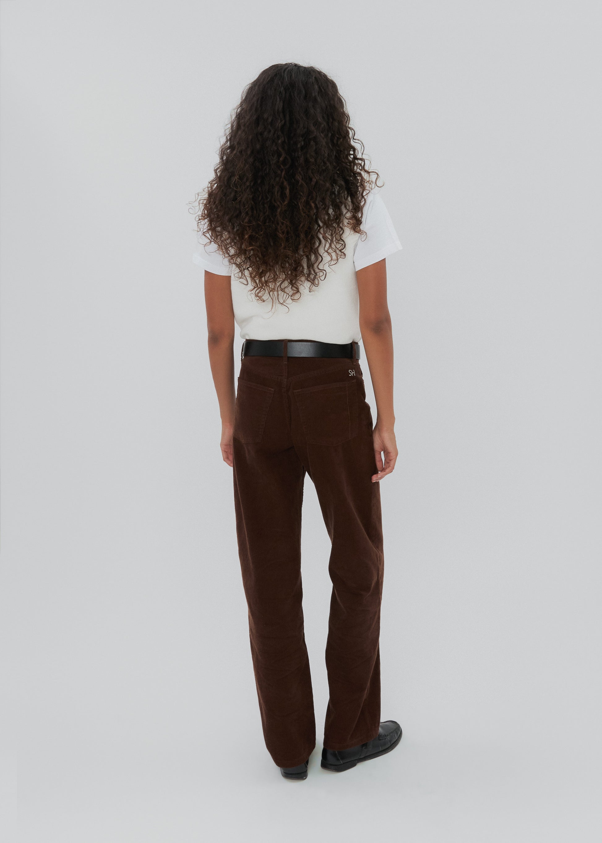 Person wearing brown pants and a white shirt on a plain background